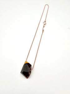 Necklace with a dark gemstone looking wood pendant on a Rose a rosegold bead chain with white background