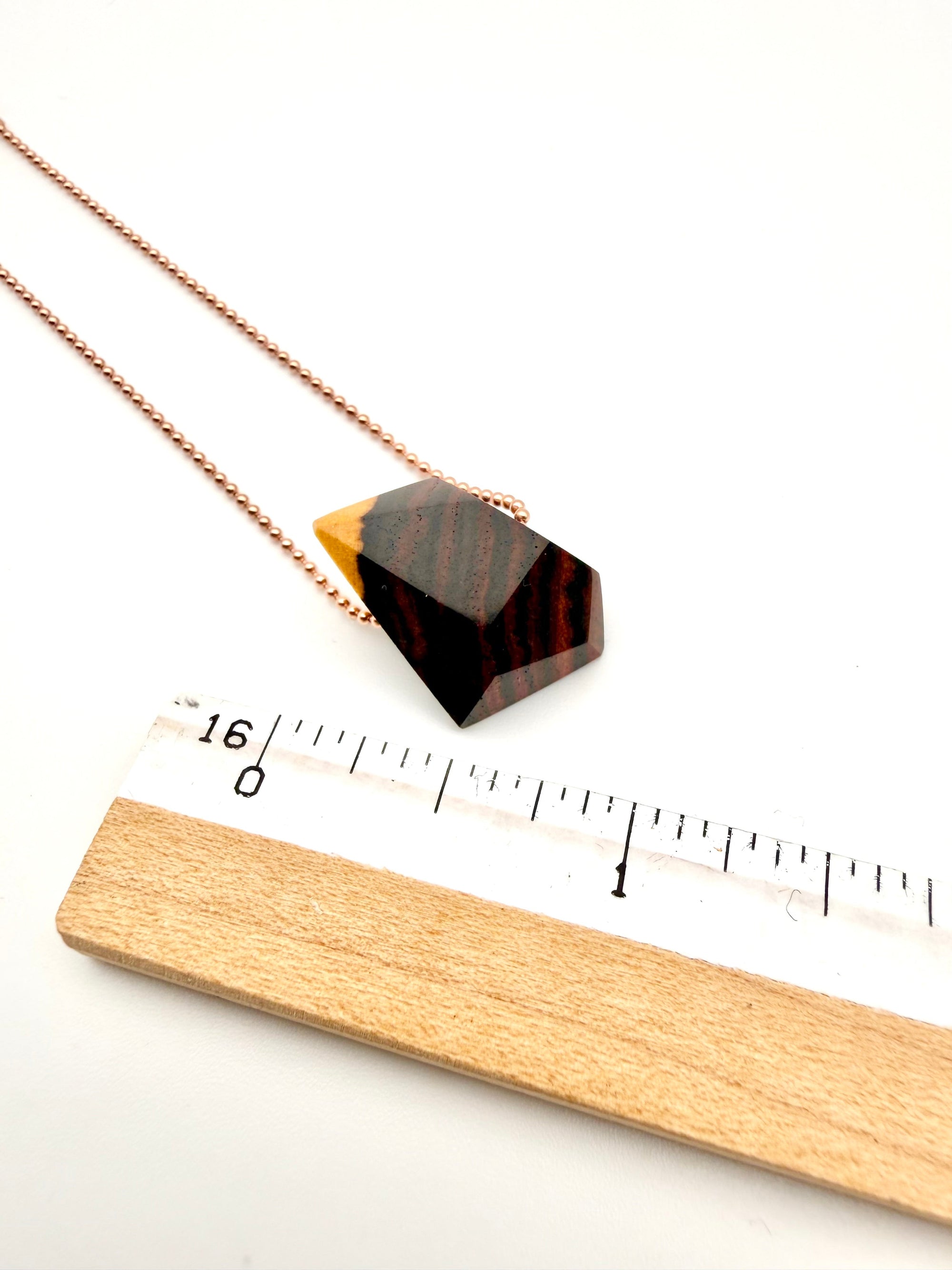 Necklace with a geometric wood pendant next to a ruler on a white background