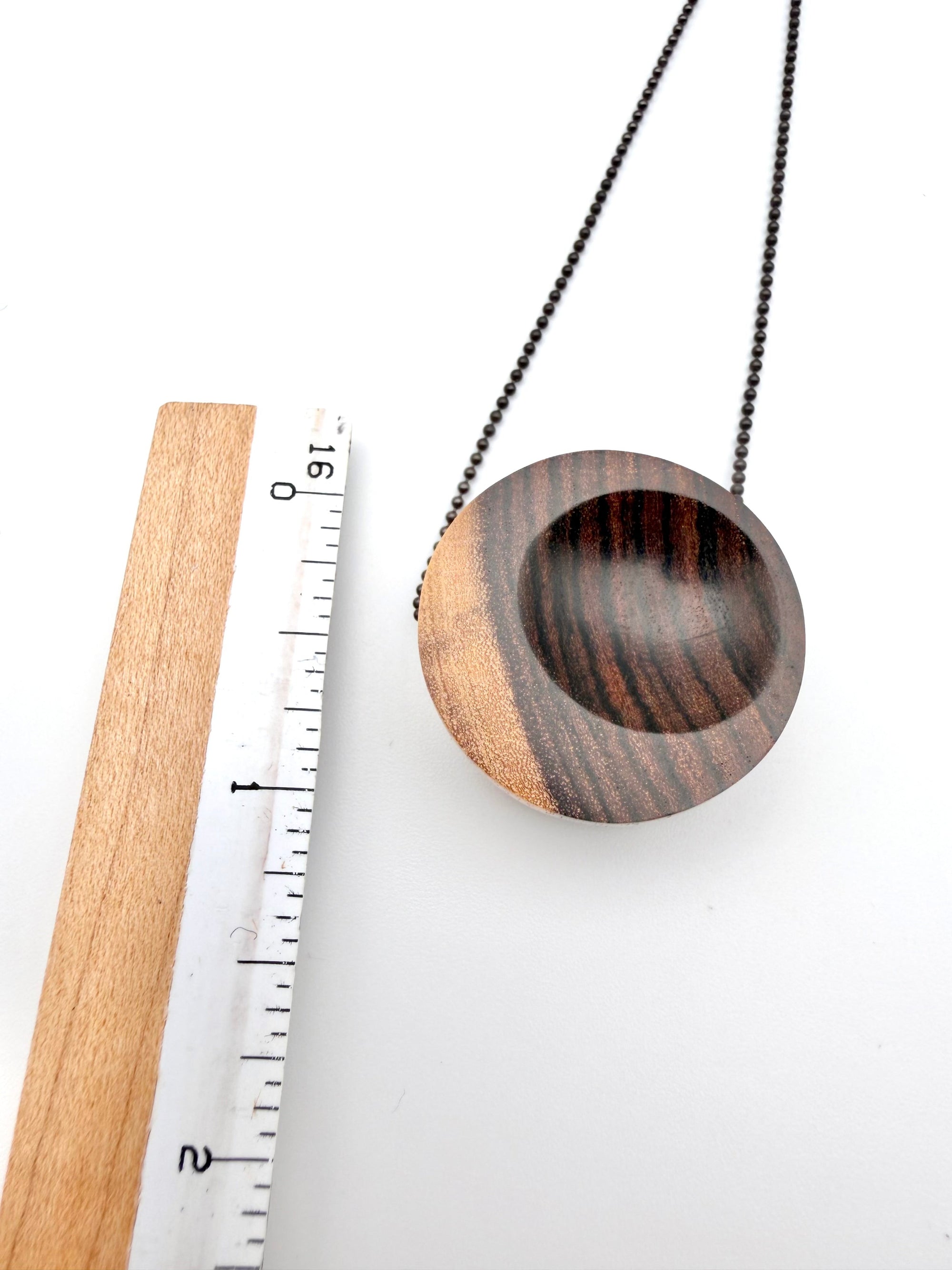 Wooden pendant with chain next to a ruler on a white background