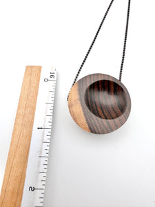 Wooden pendant with chain next to a ruler on a white background