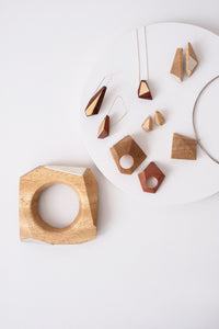 Wooden geometric objects that can be worn as jewelry with silver accents on a white circle set on a white background. 