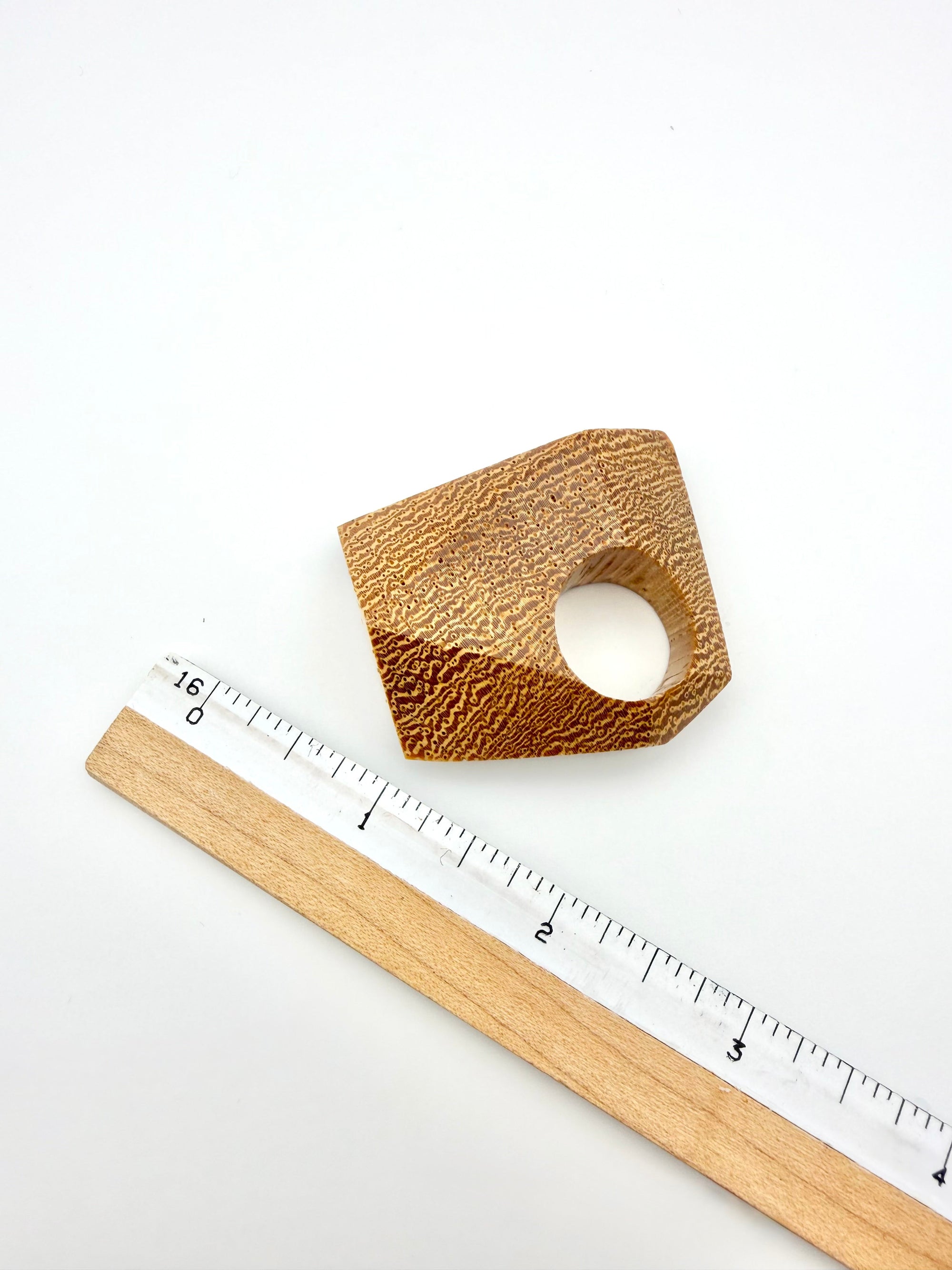 Wooden ring with a textured surface next to a ruler on a white background