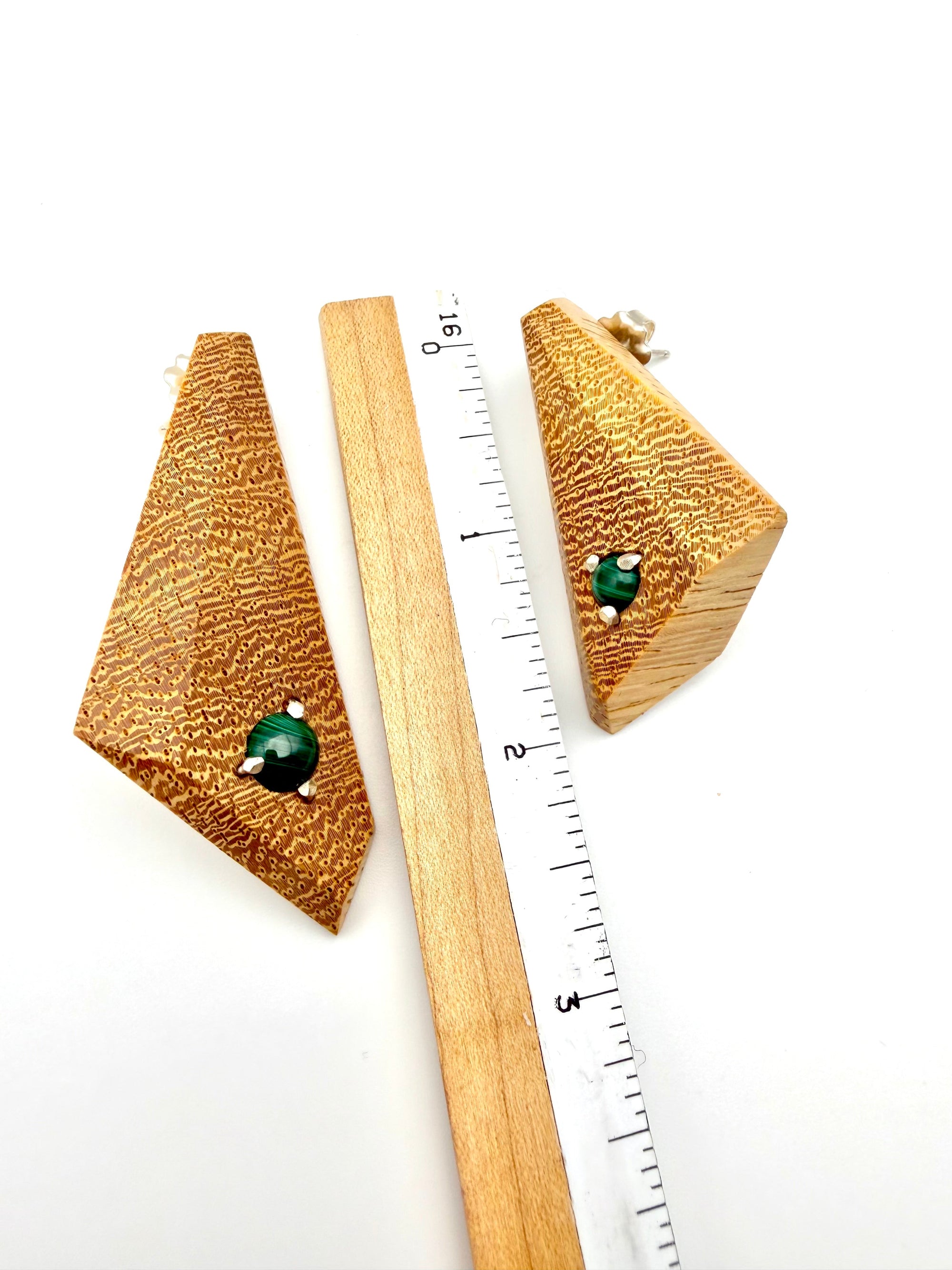 Blonde wood triangle-shaped earrings with Malachite gemstones set with silver with ruler for scale on a white background
