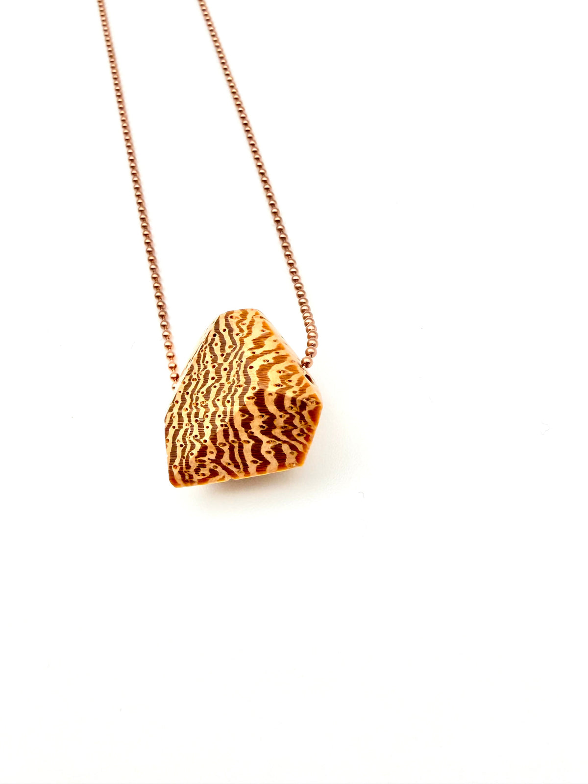 Blonde wood pendant with a dramatic grain pattern on rose gold ball chain on a white background