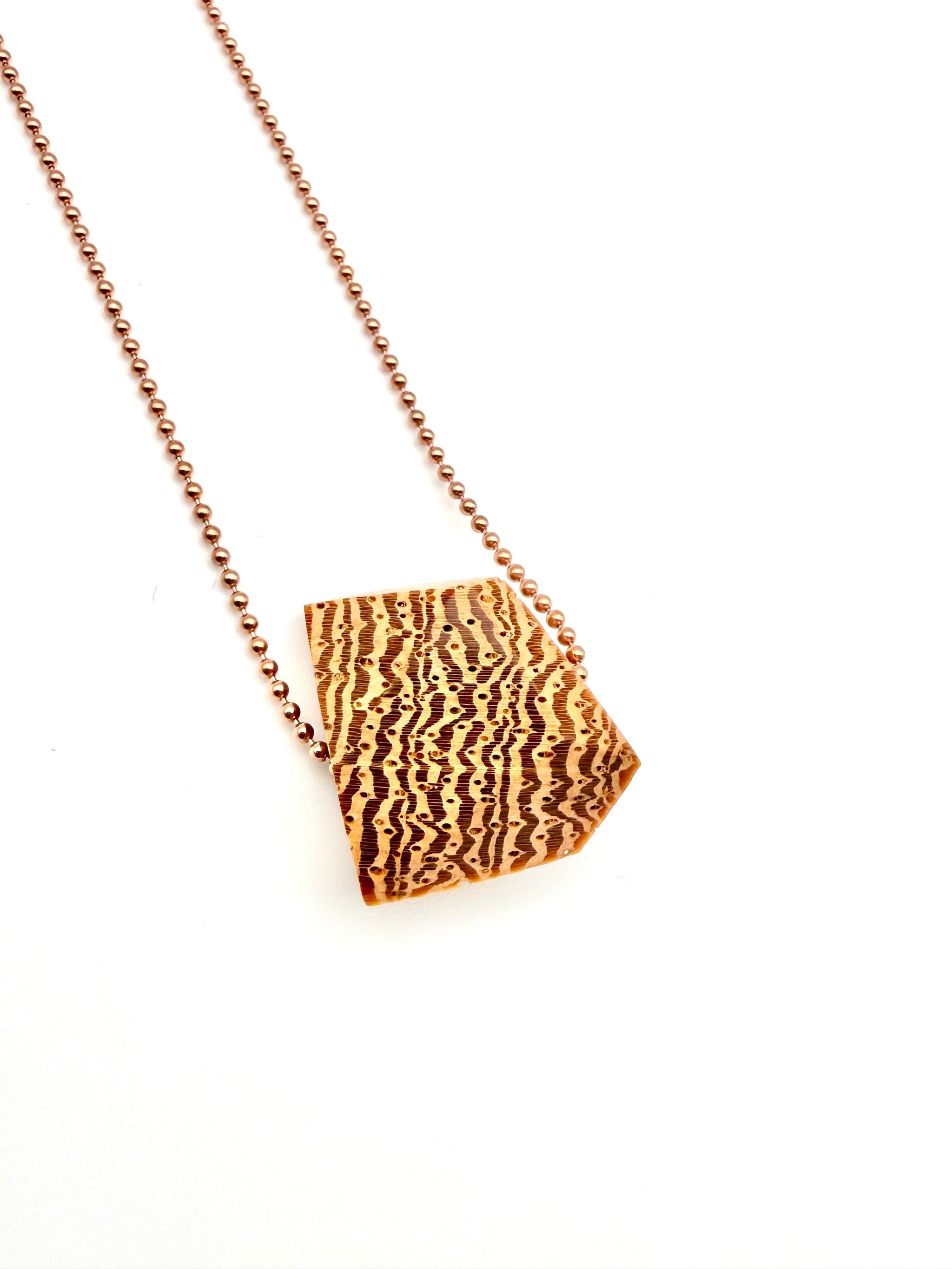 Blonde wood pendant with a dramatic grain pattern on rose gold ball chain on a white background