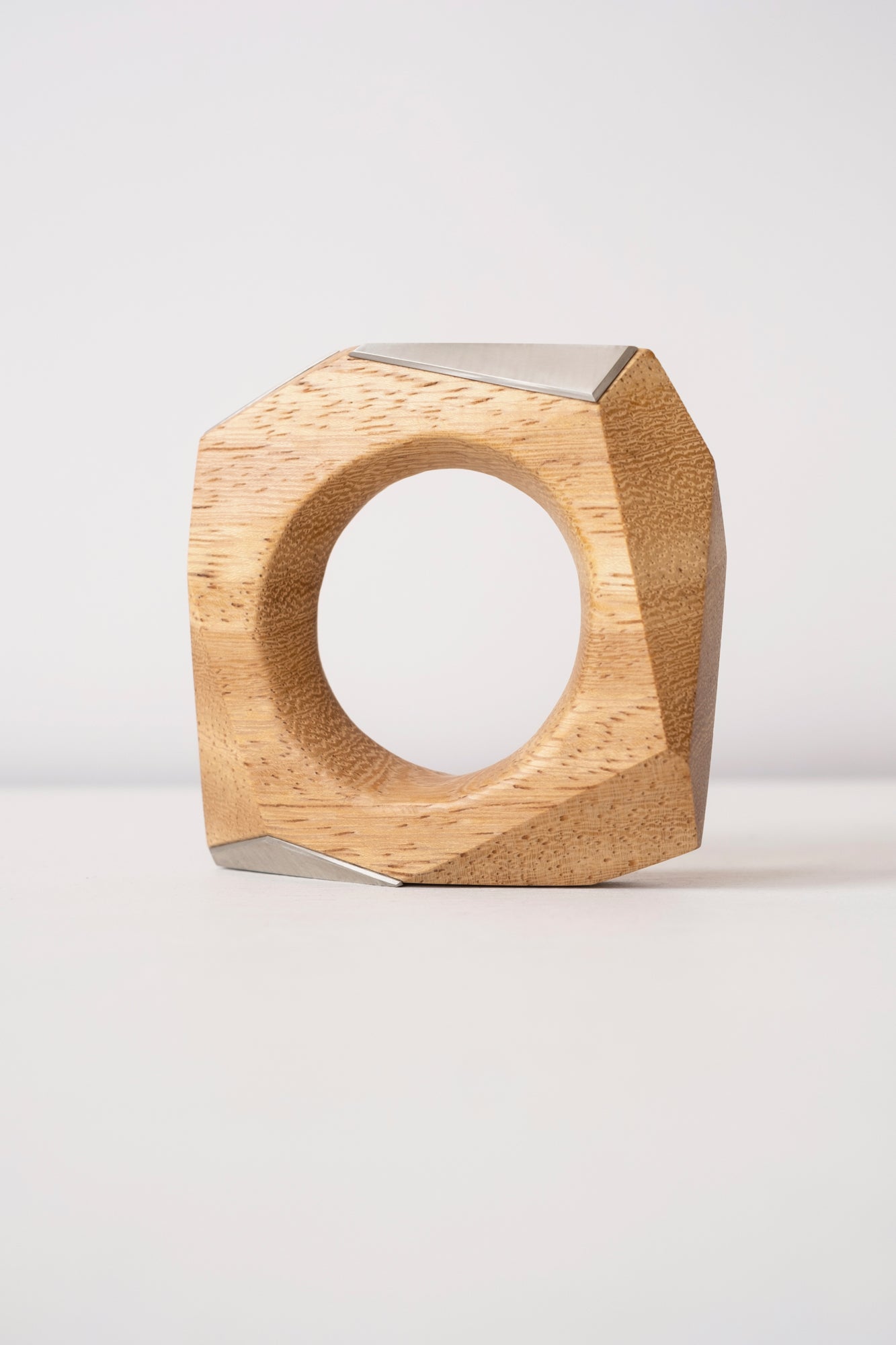 Blonde wood geometric object that can be worn as a bangle with silver accents on a white background