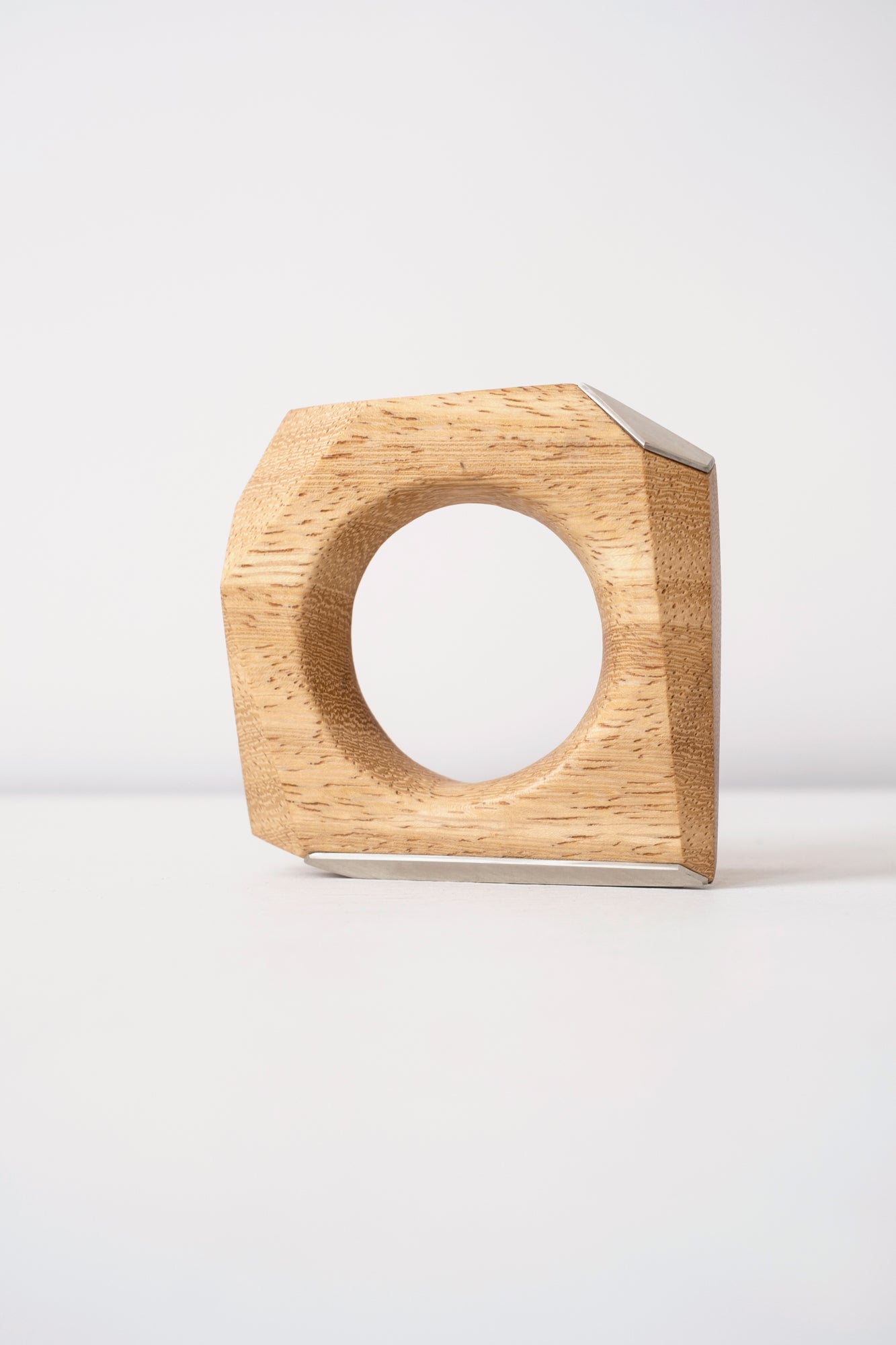 Wooden geometric object that can be worn as a bangle with silver accents on a white background