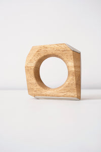 Wooden geometric object that can be worn as a bangle with silver accents on a white background