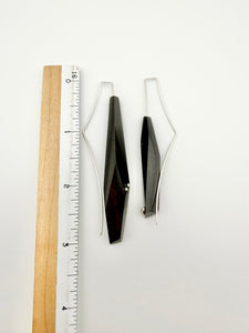 Long Geometric pair of wood earrings with black and silver design next to a ruler on a white background