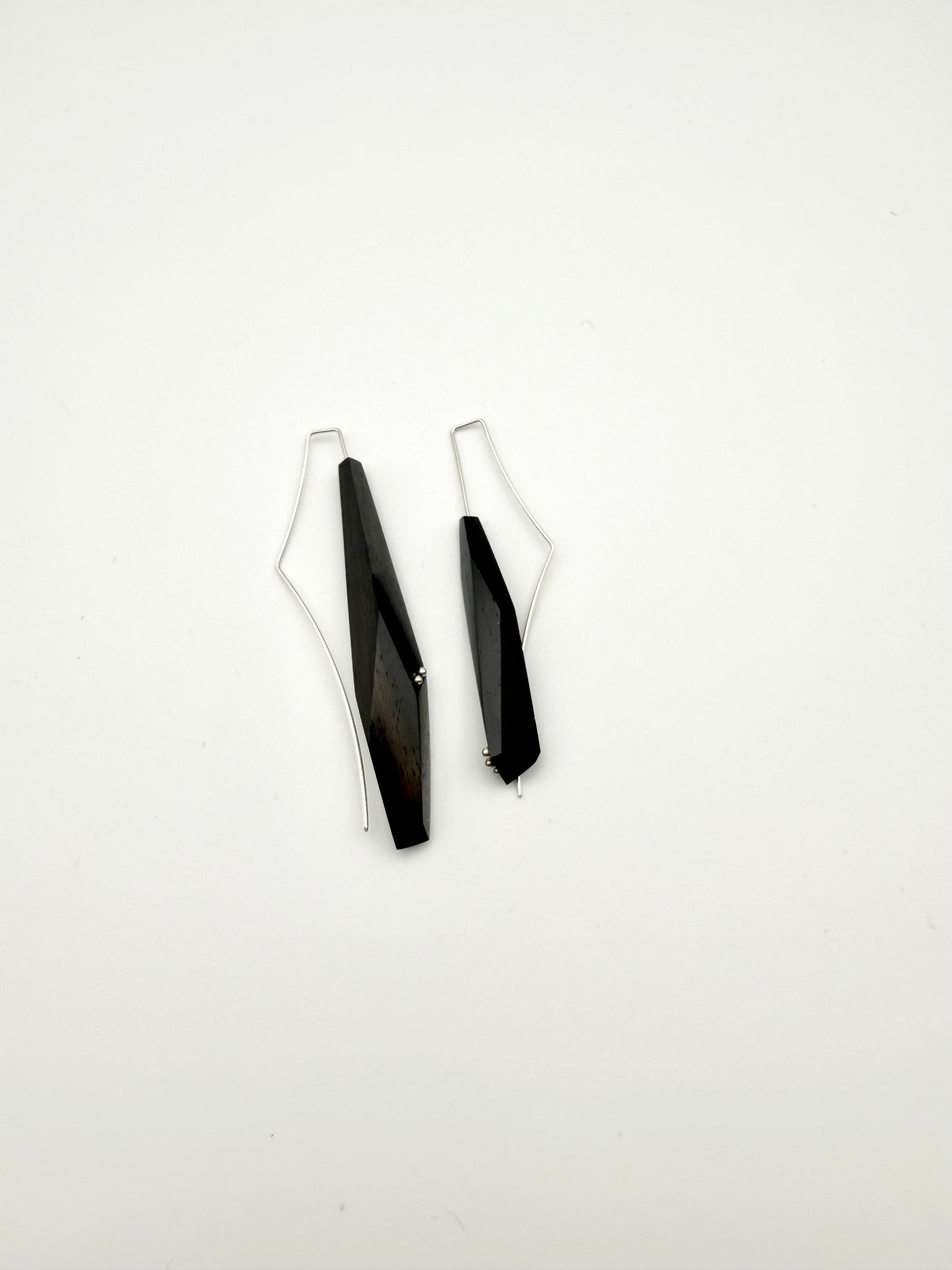 Side View of long black asymmetric geometric pair of wood earrings with silver ear wires and dot details on a white background.
