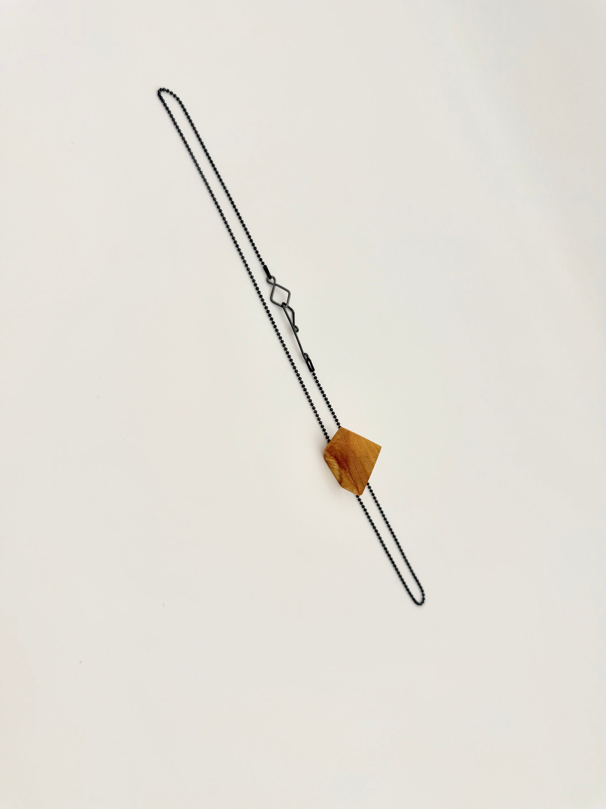 Geometric olivewood pendant on an oxidized silver chain with custom clasp on white background. 
