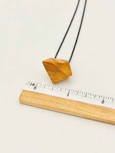 Geometric olivewood pendant on an oxidized silver chain next to ruler for scale on white background
