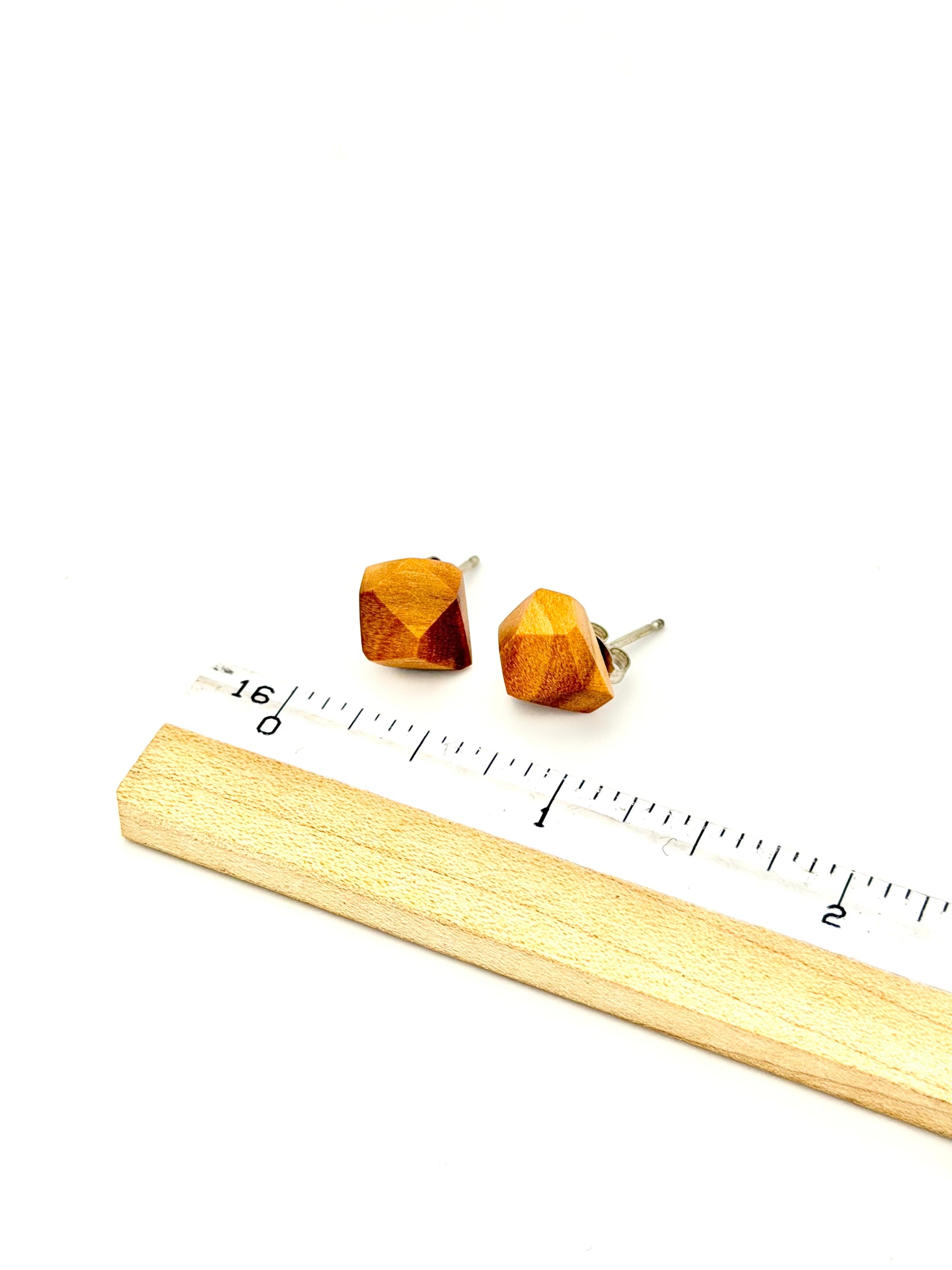 Wooden geometric earrings with a ruler for scale on a white background
