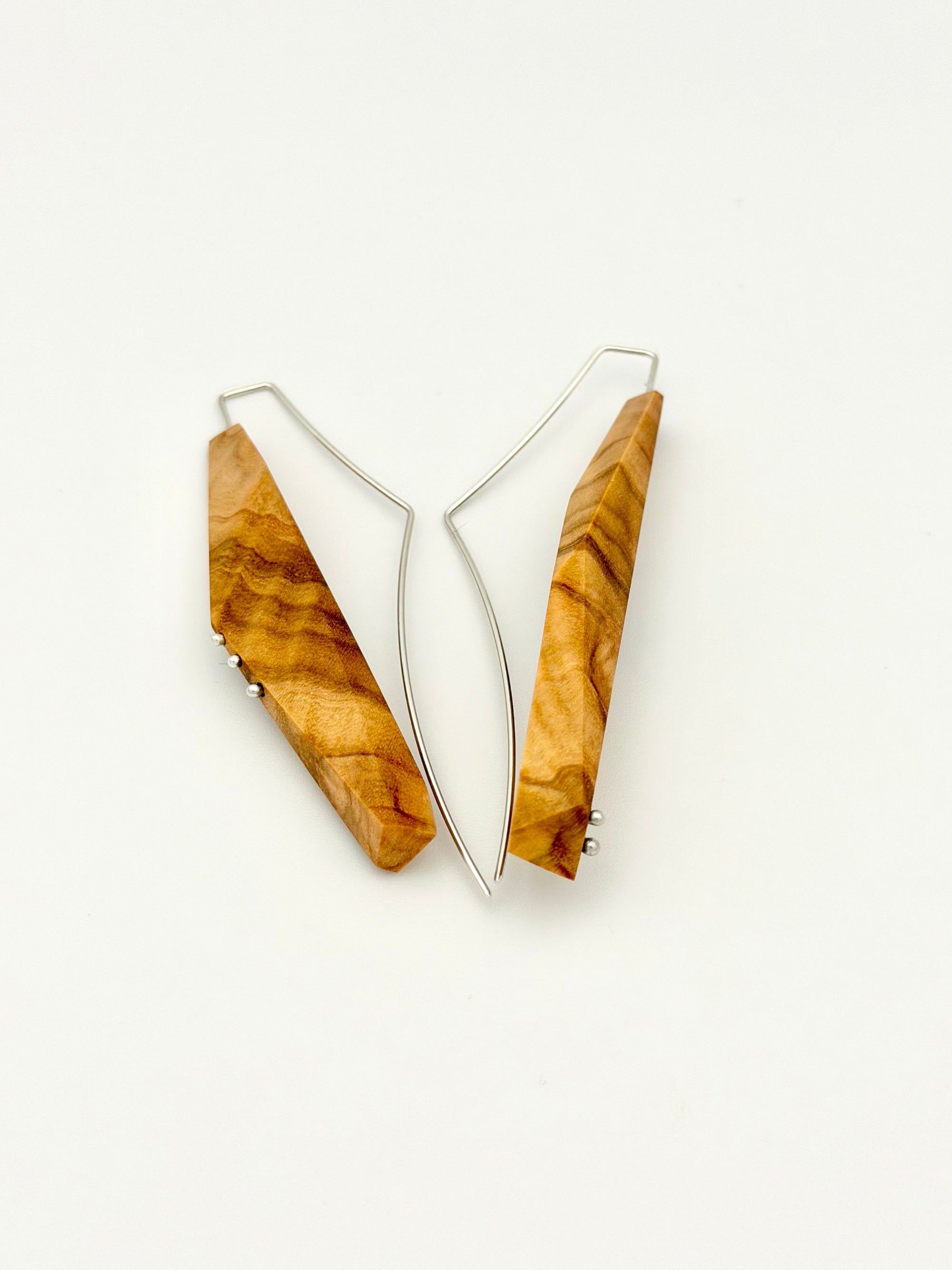 Olivewood asymmetric long narrow earrings with silver details and long web like ear wires on white background. 
