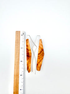 Olivewood asymmetric long narrow earrings with silver details next to ruler for scale on white background. 