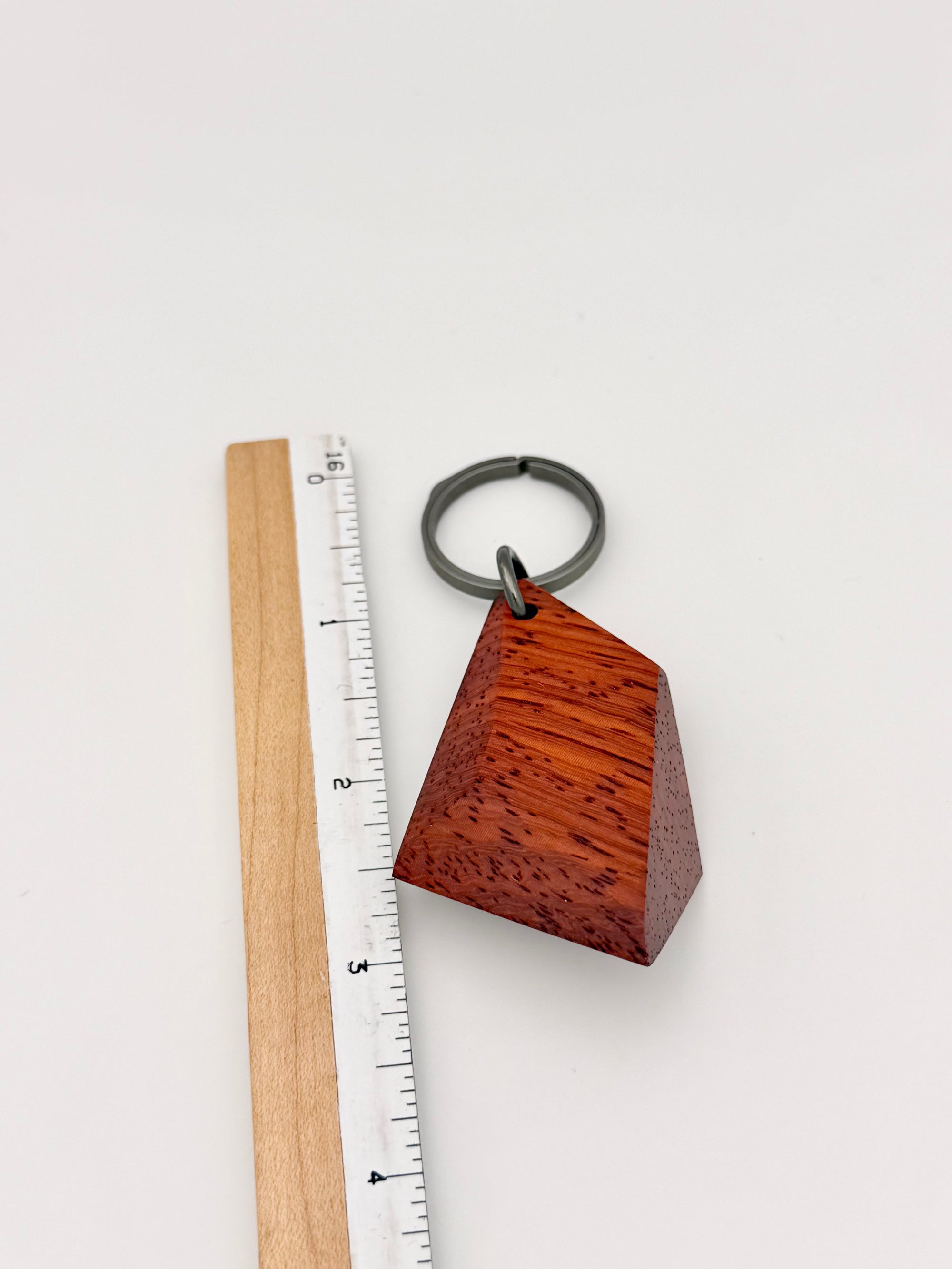 Wooden geometric keychain next to a ruler on a white background