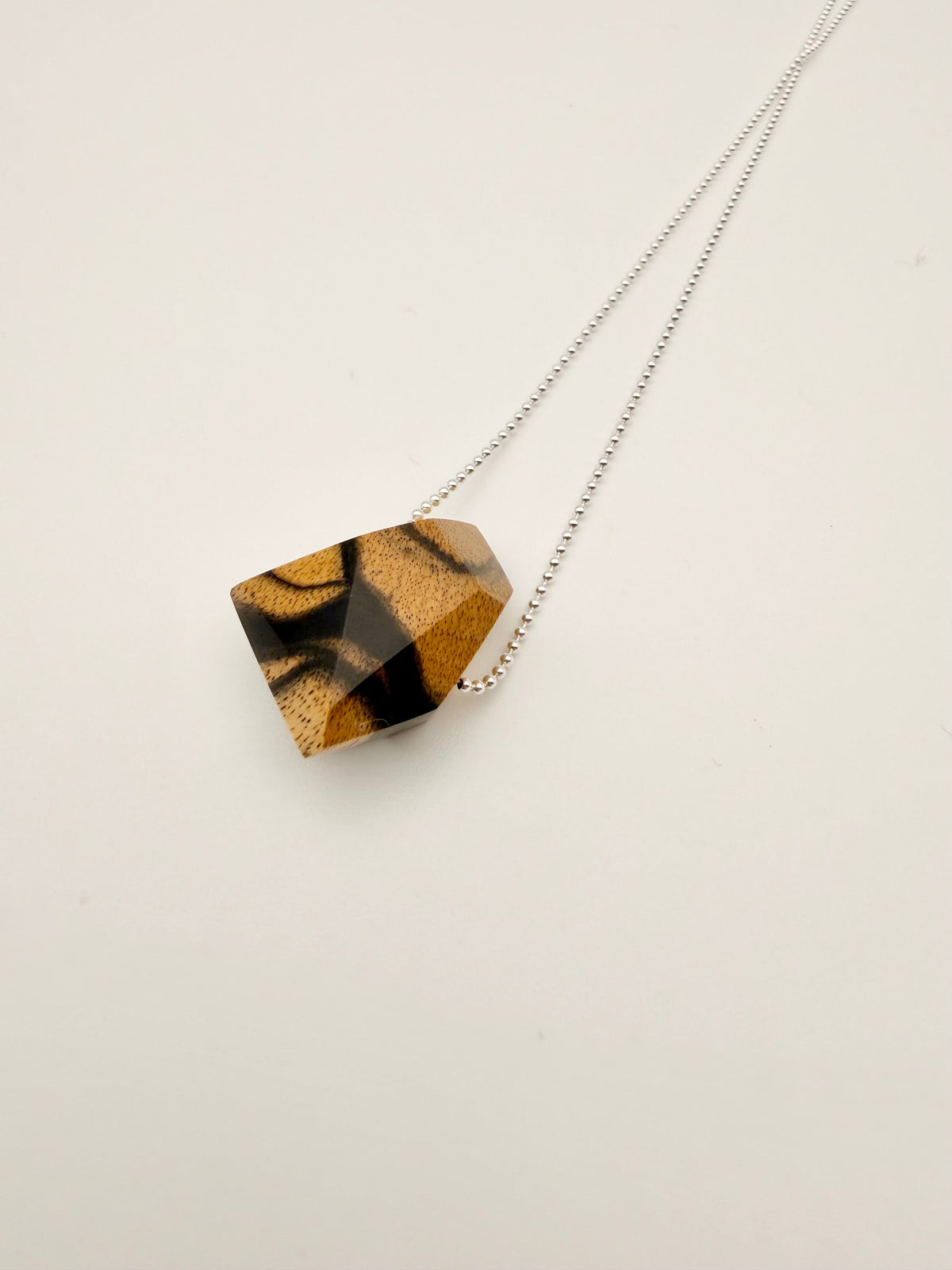 Necklace with a geometric polished wood pendant on a silver bead chain and light background