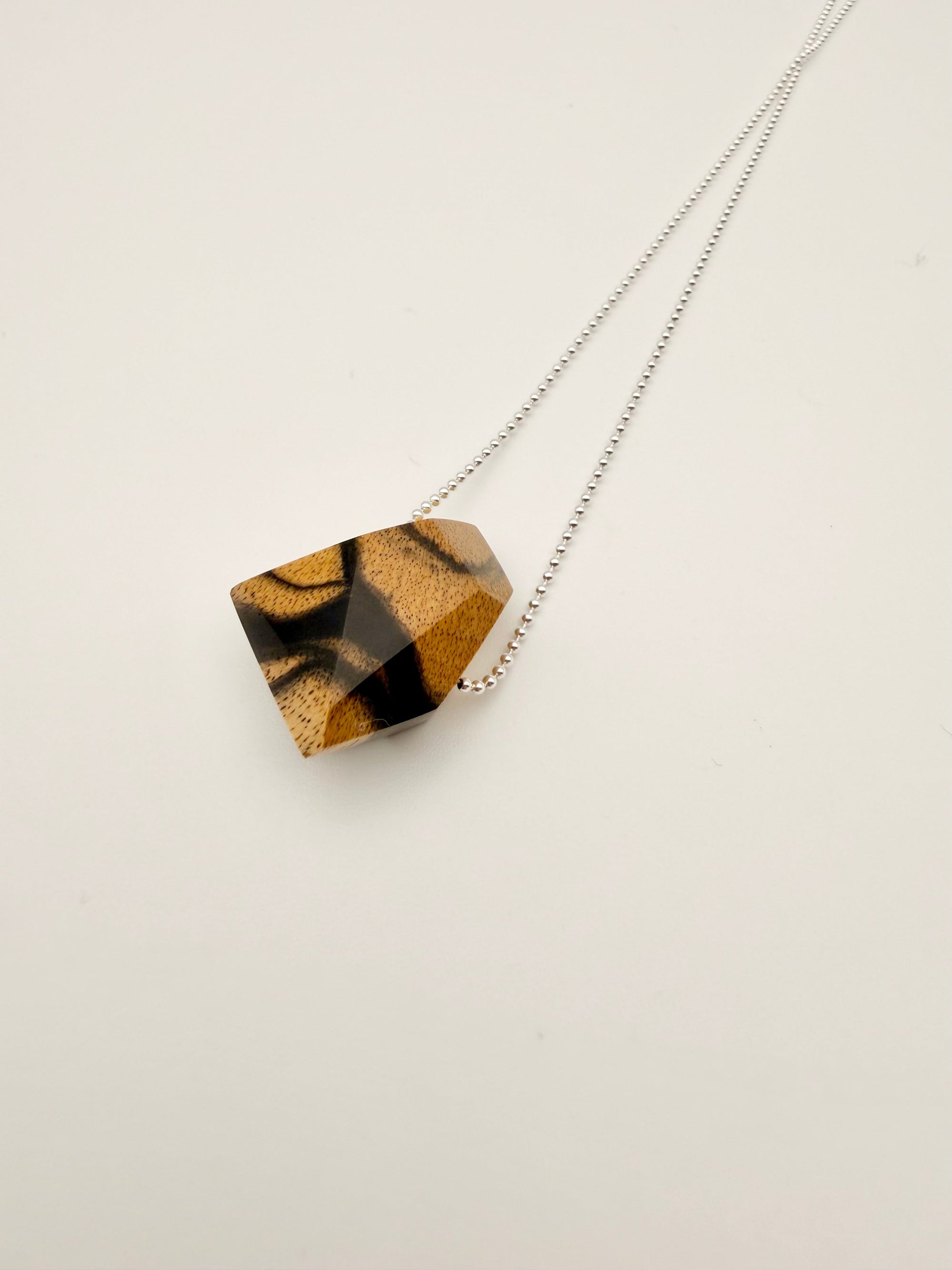 Necklace with a geometric polished wood pendant on a silver bead chain and light background