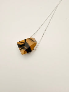 Necklace with a geometric polished wood pendant on a silver bead chain and light background