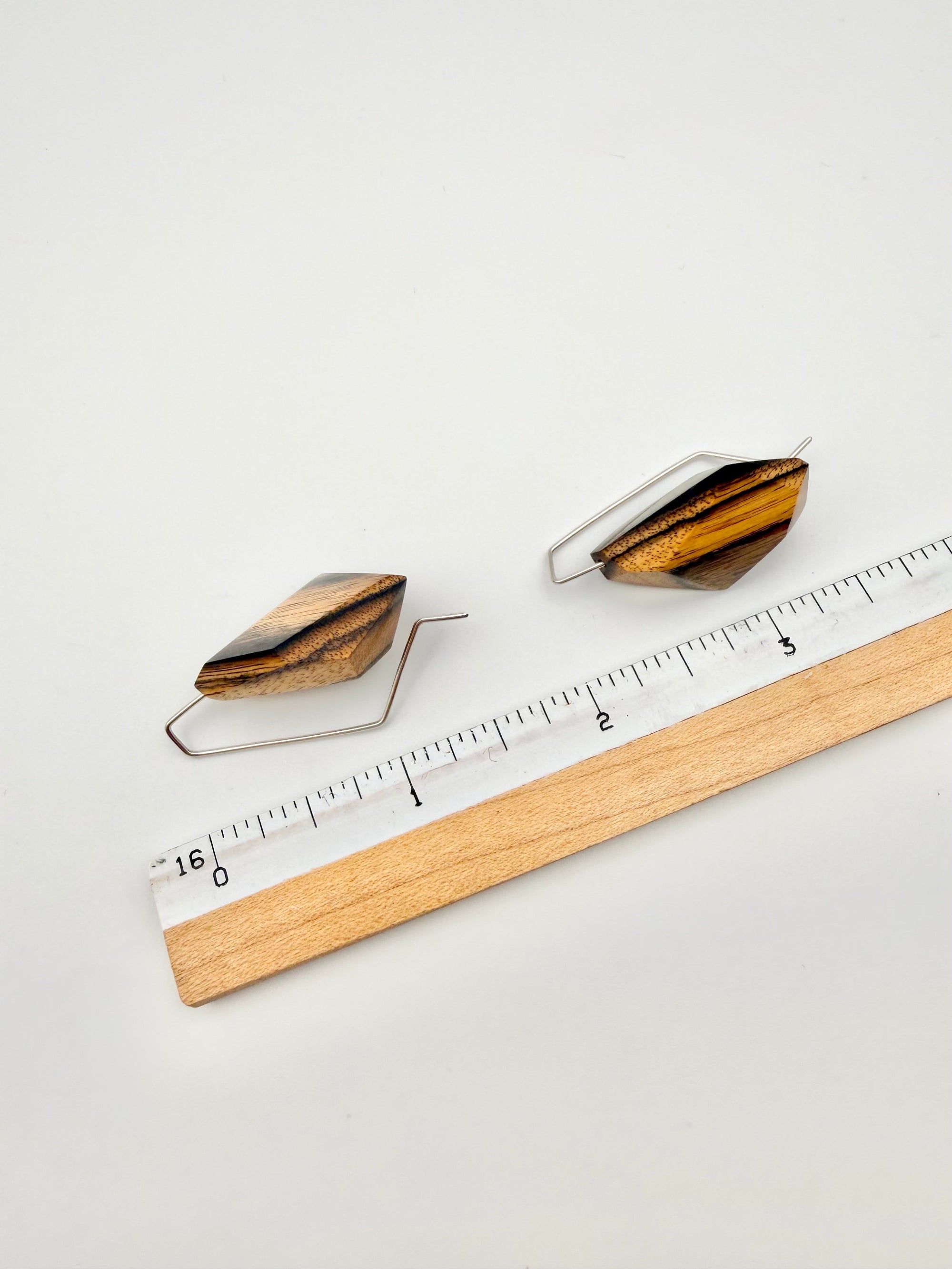 Wooden earrings next to a ruler for scale on a white background