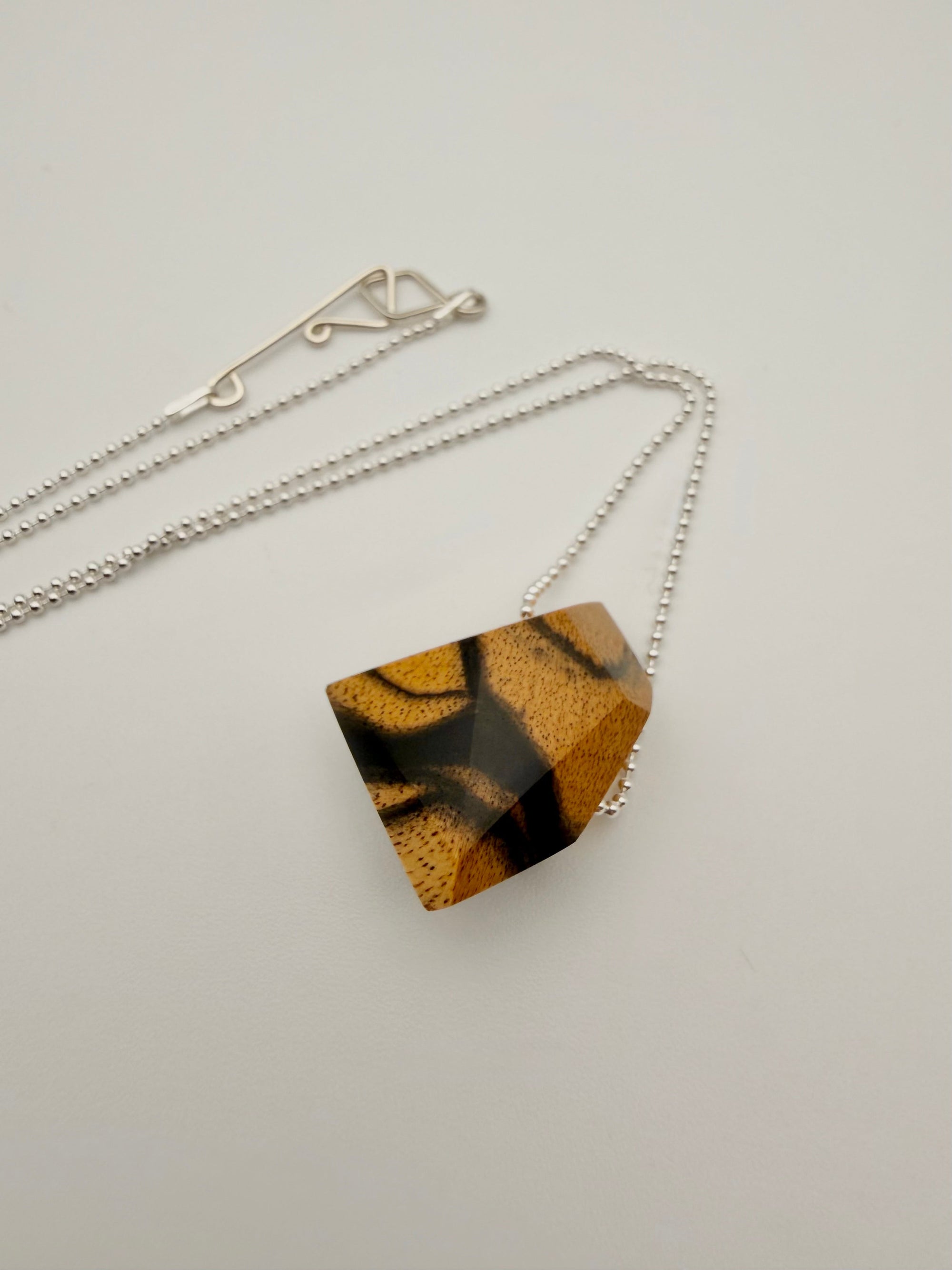 Necklace with a geometric polished wood pendant (resembling a stone) on a silver bead chain and light background