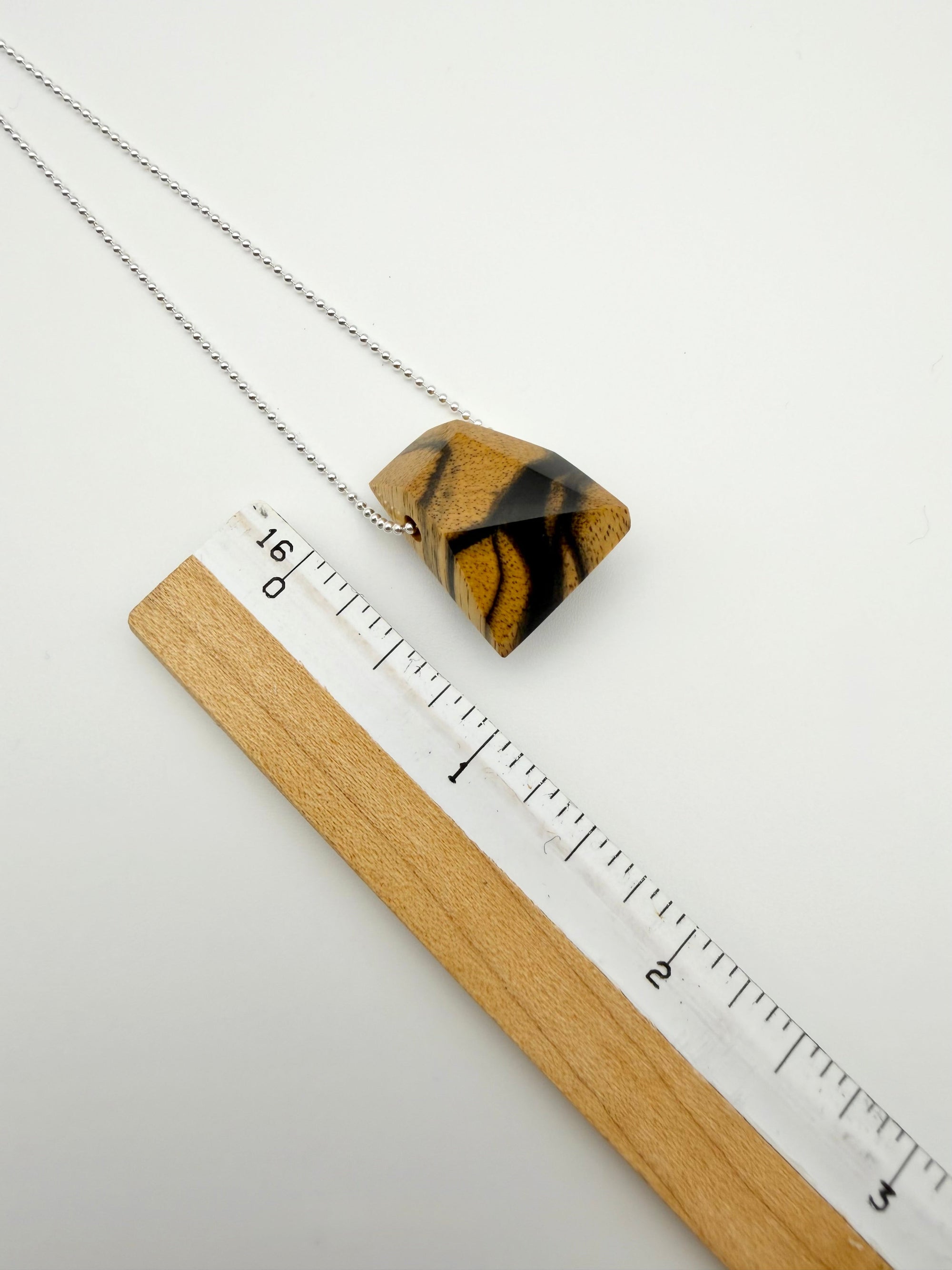 Necklace with a geometric polished Black & White ebony wood pendant next to ruler for scale. Pendant is a littler smaller than an inch. 