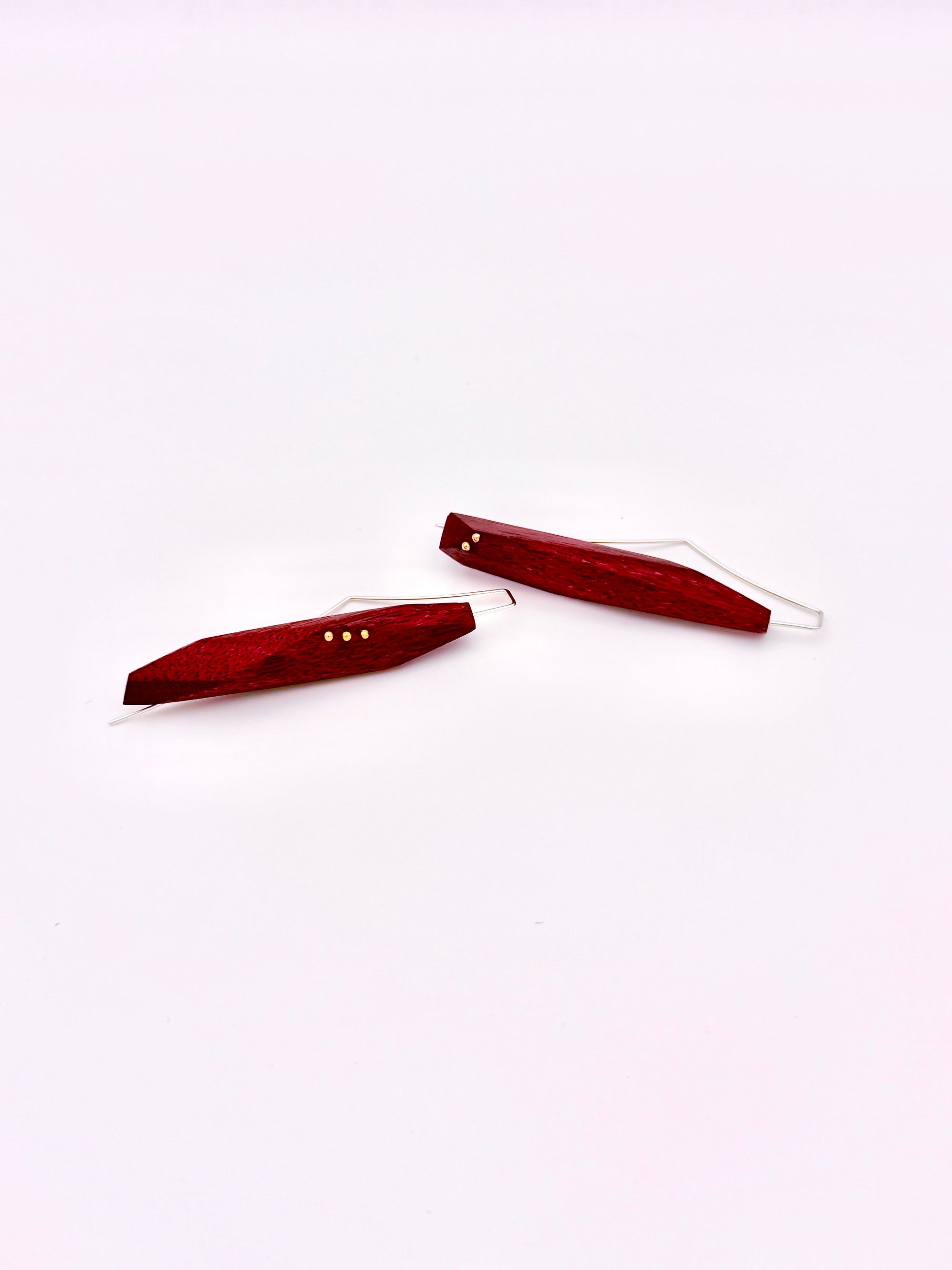 Purple heart wood earrings with silver ear wires on their sides on a white background. 