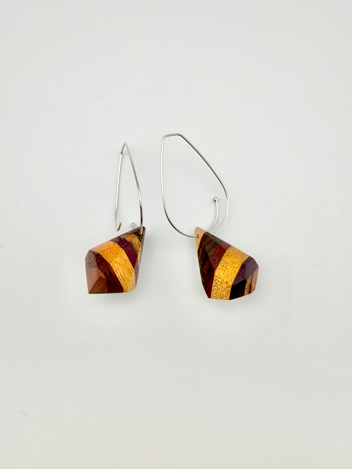 layers of wood shaped into geometric nuggets threaded onto a silver teardrop hoop earrings on a white background