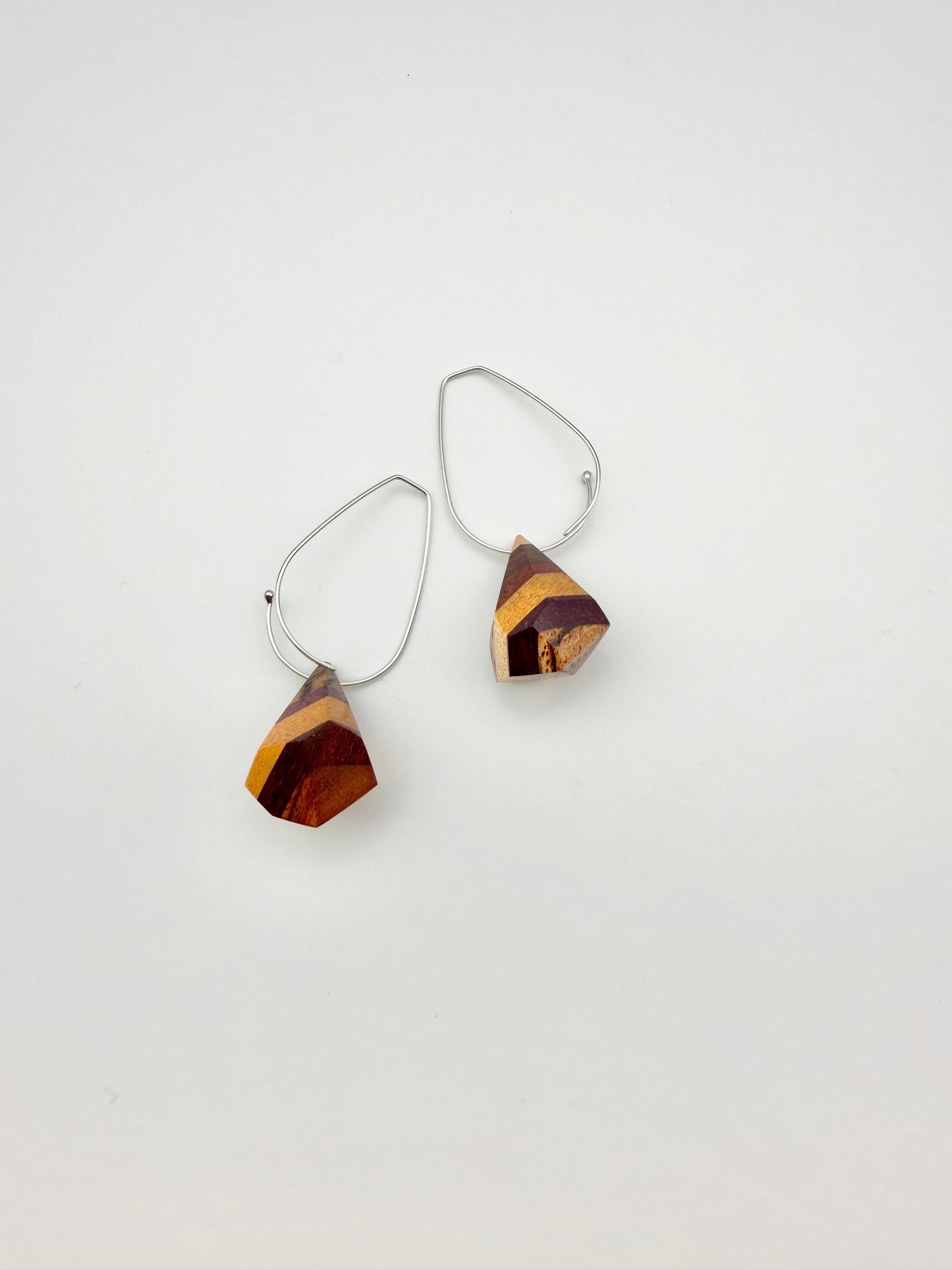 layers of wood shaped into geometric nuggets threaded onto a silver teardrop hoop earrings on a white background

