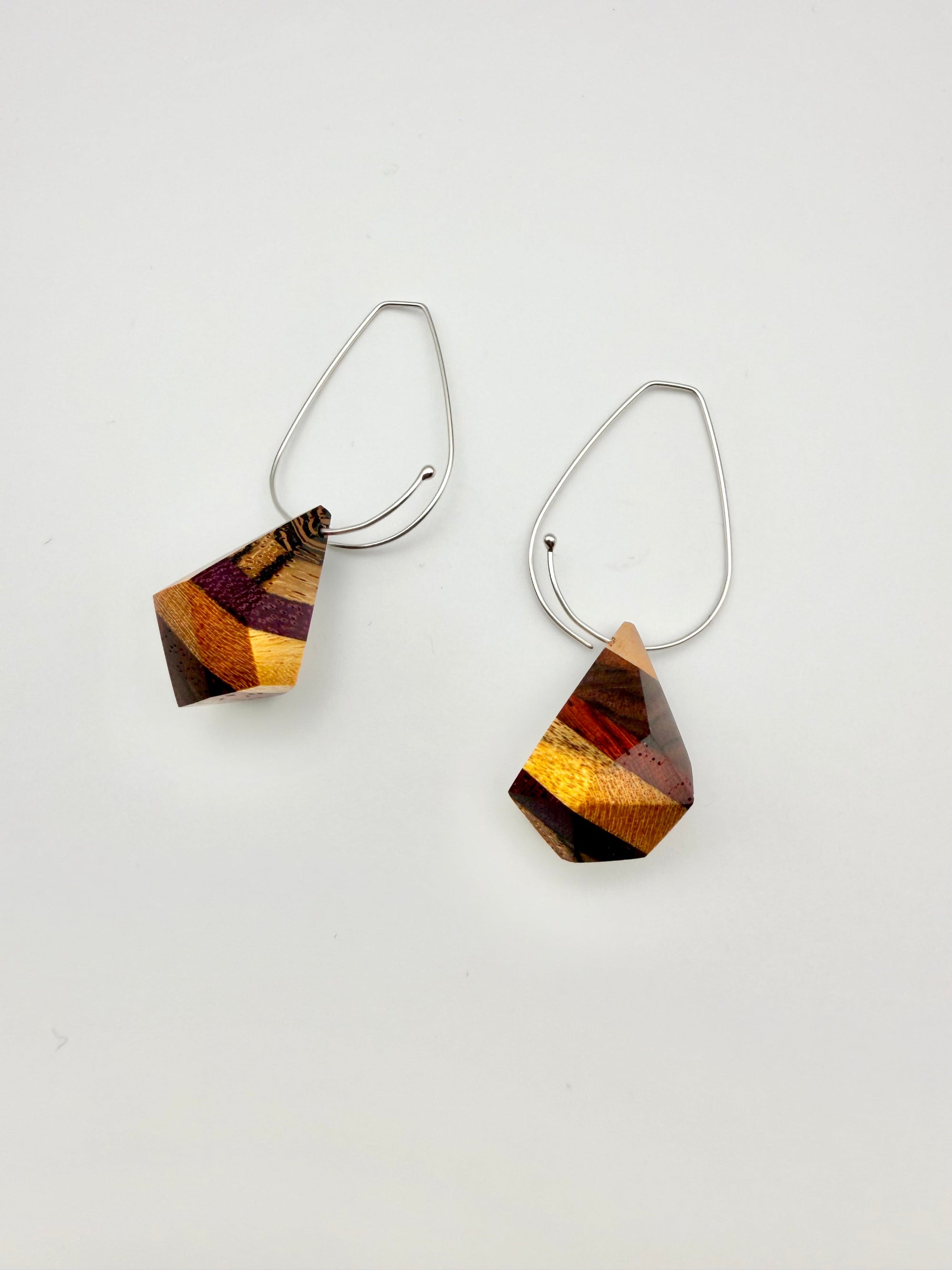 layers of wood shaped into geometric nuggets threaded onto a silver teardrop hoop earrings on a white background