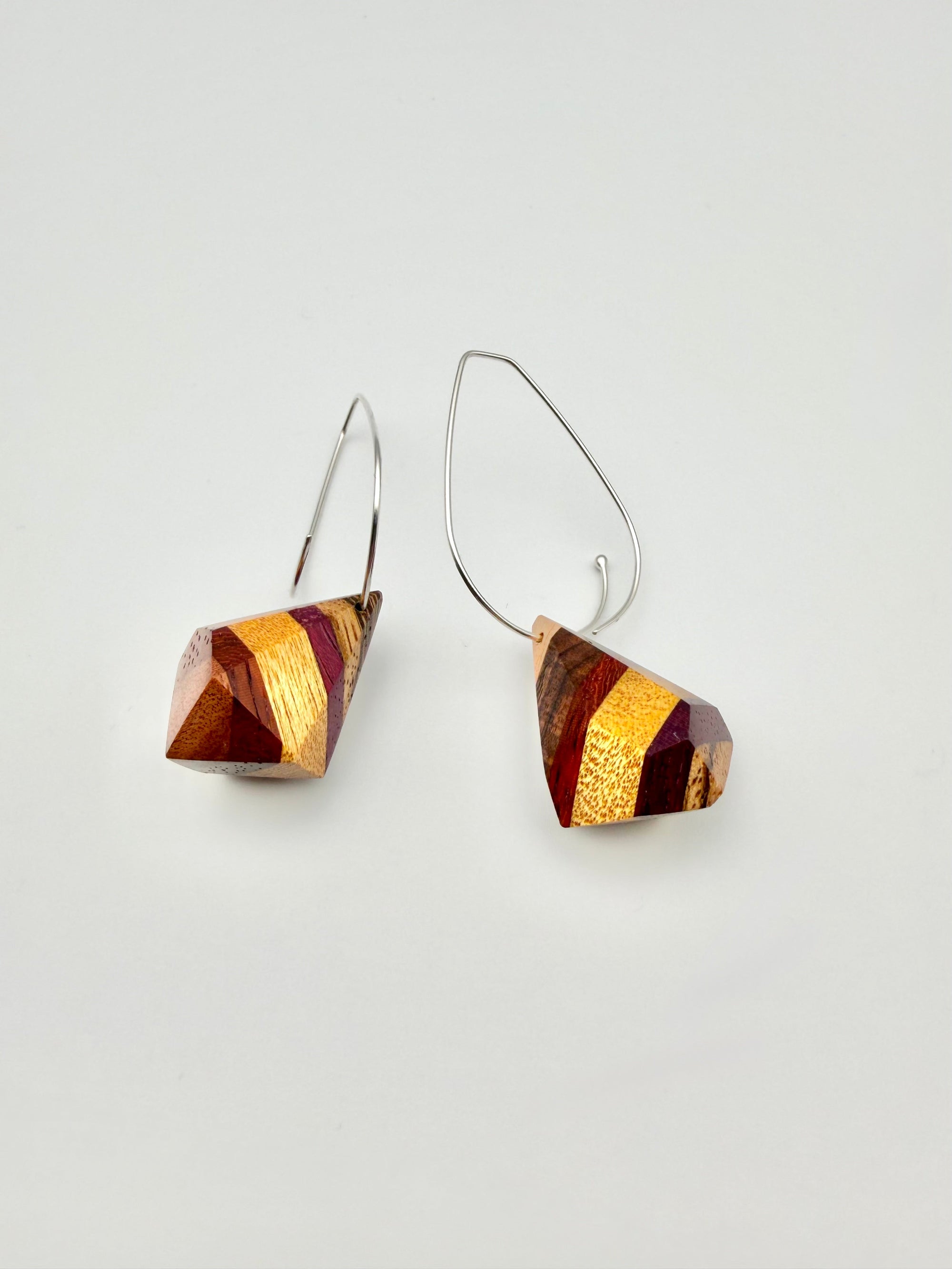 layers of wood shaped into geometric nuggets threaded onto a silver teardrop hoop earrings on a white background