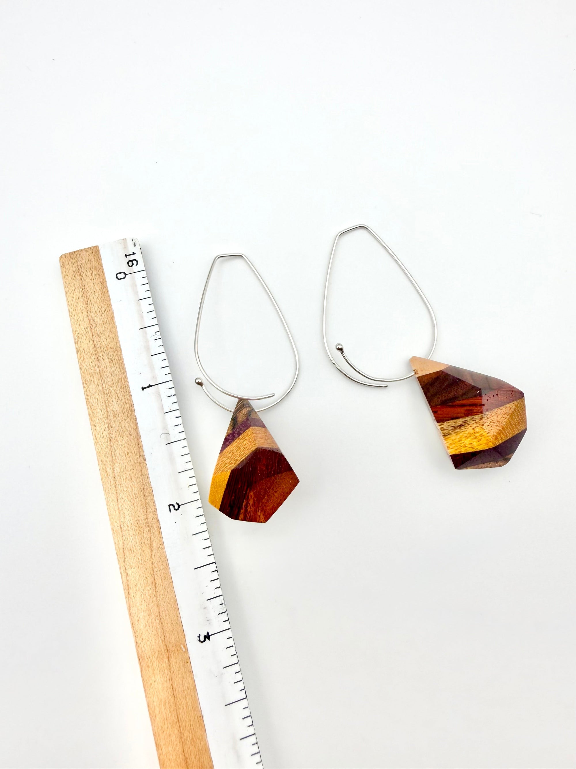 layers of wood shaped into geometric nuggets threaded onto a silver teardrop hoop earrings on a white background