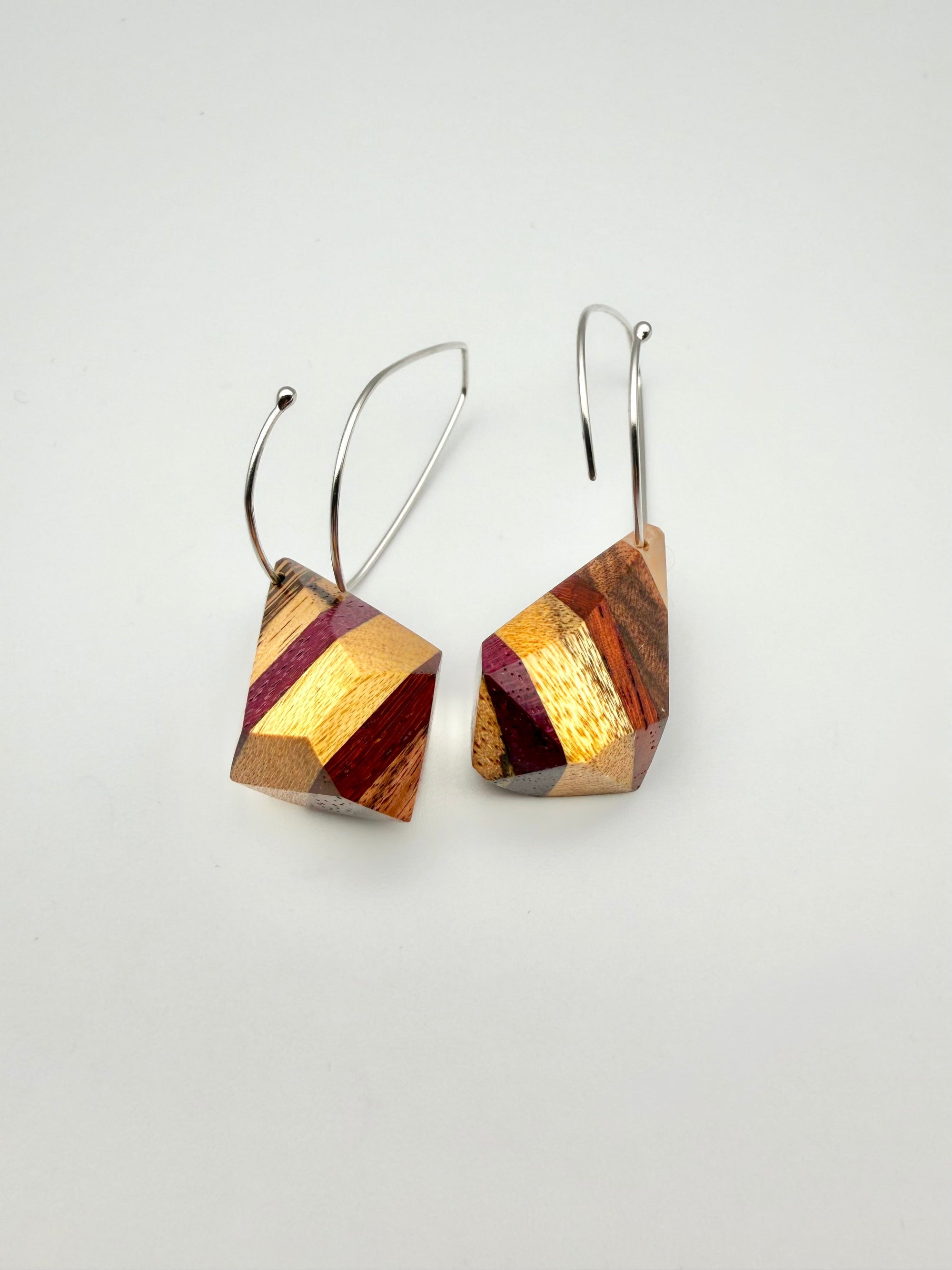 layers of wood shaped into geometric nuggets threaded onto a silver teardrop hoop earrings on a white background