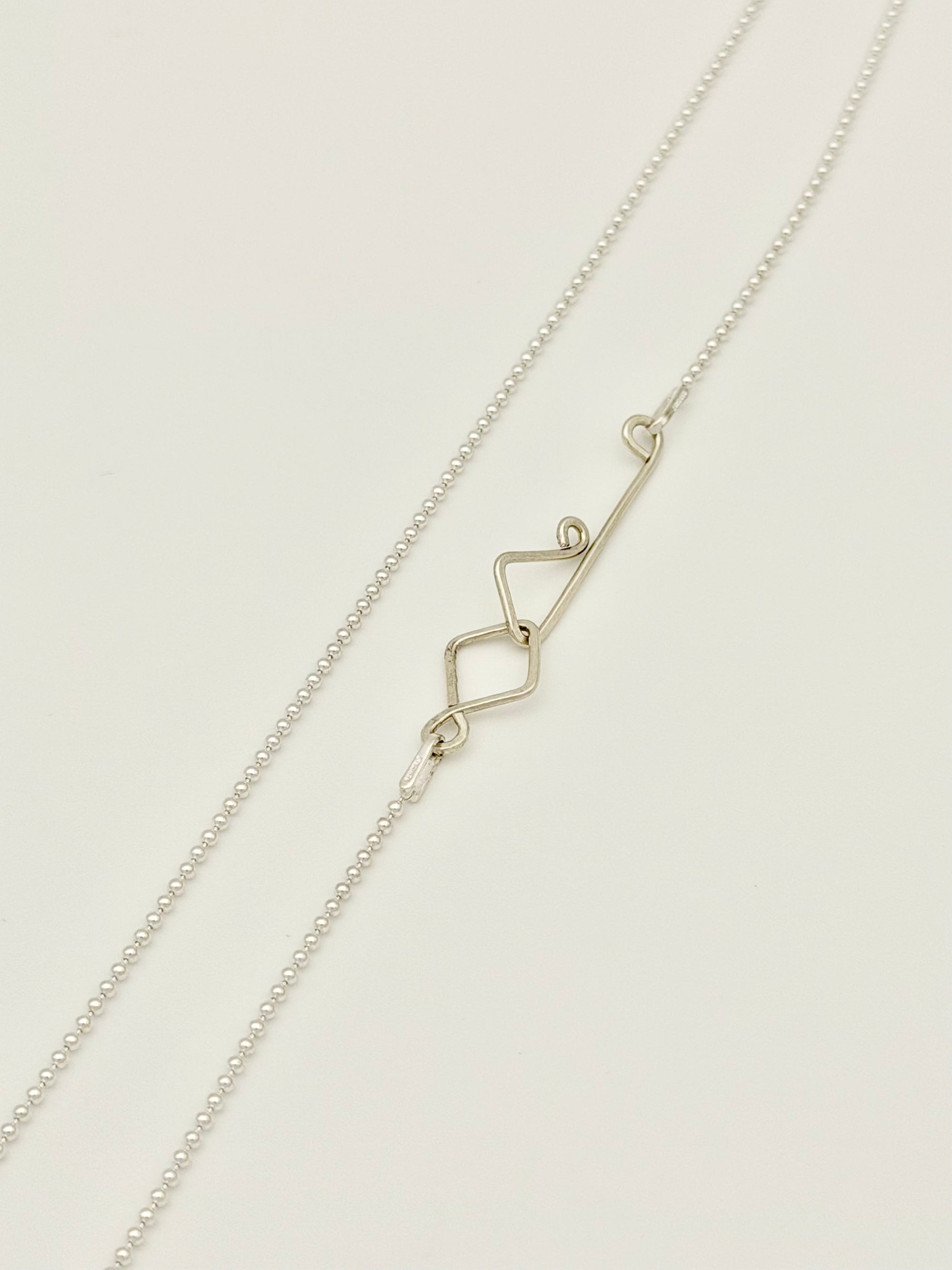 Silver bead chain with custom decorative clasp on white background. 