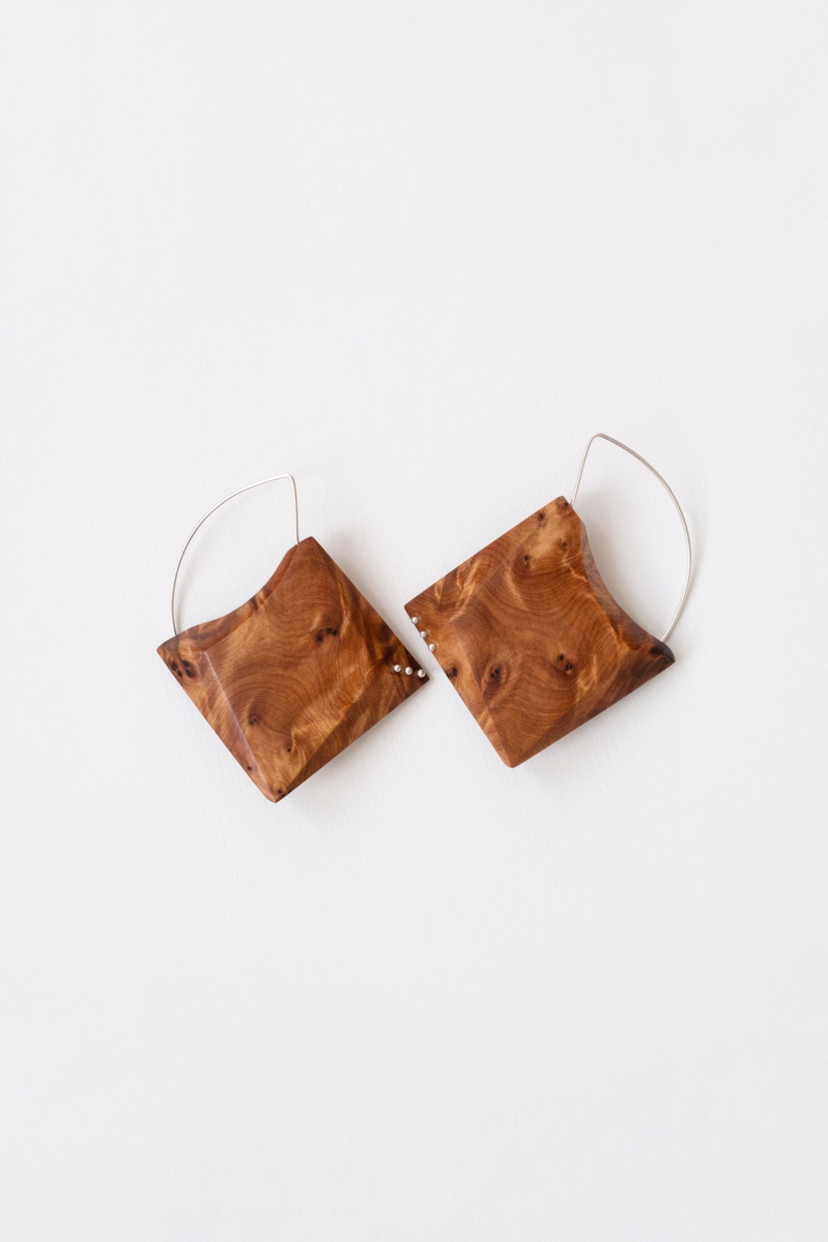 Ornate wood grain geometric earrings with Silver details and hoops on white background. 