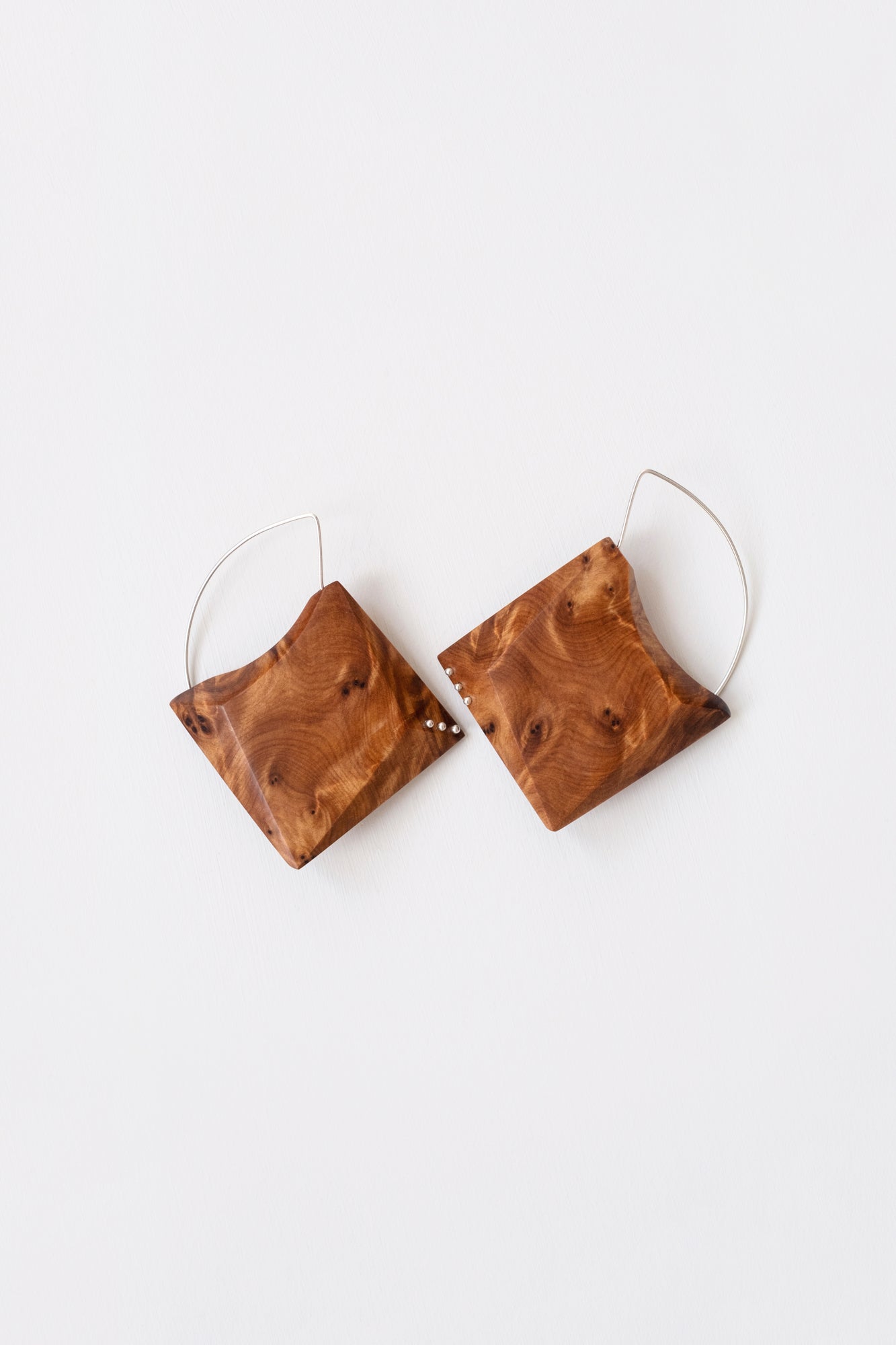 Ornate wood grain geometric earrings with Silver details and hoops on white background. 