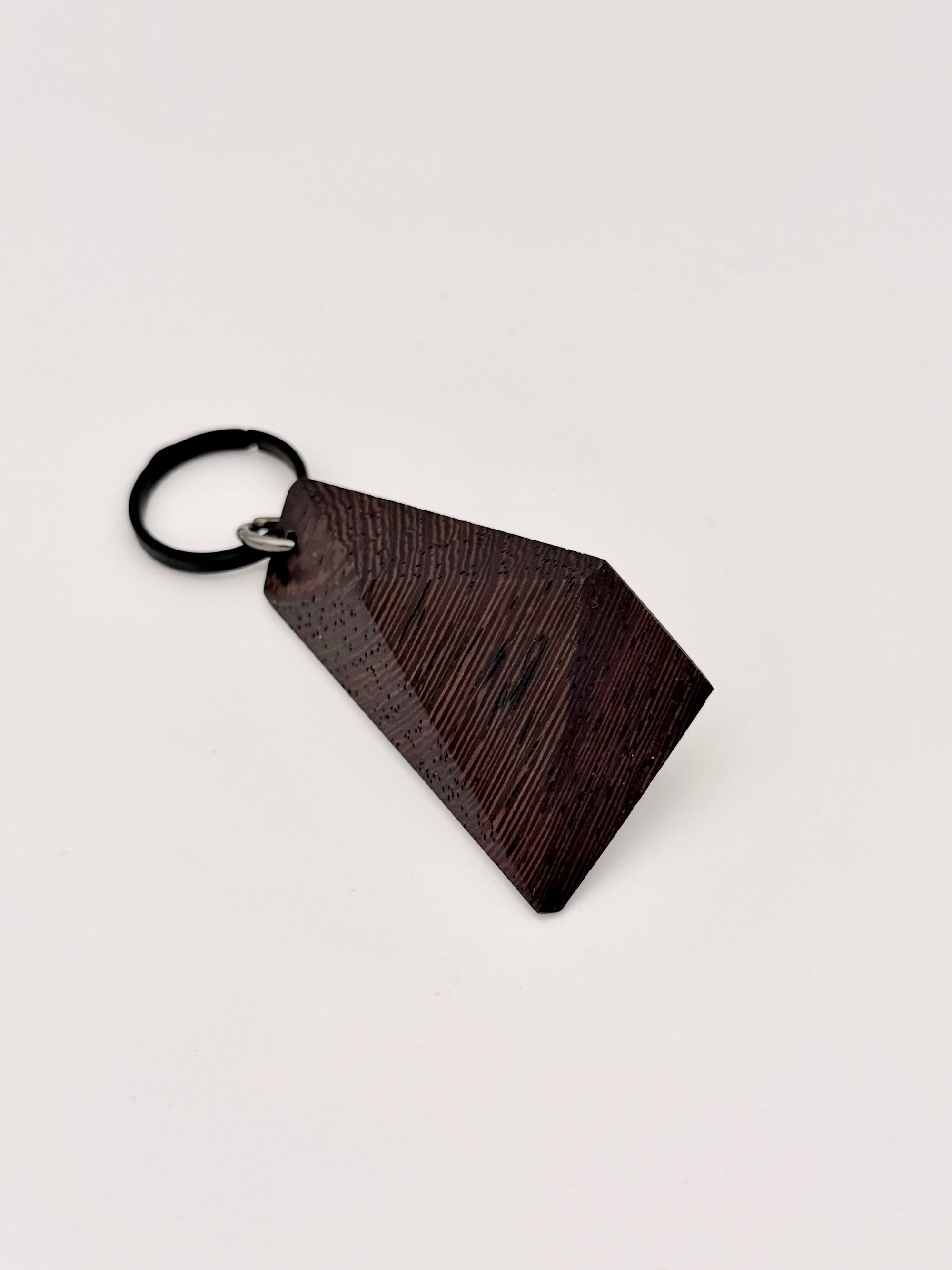 (Wenge) Dark brown and black wood keychain with geometric design on a light gray background