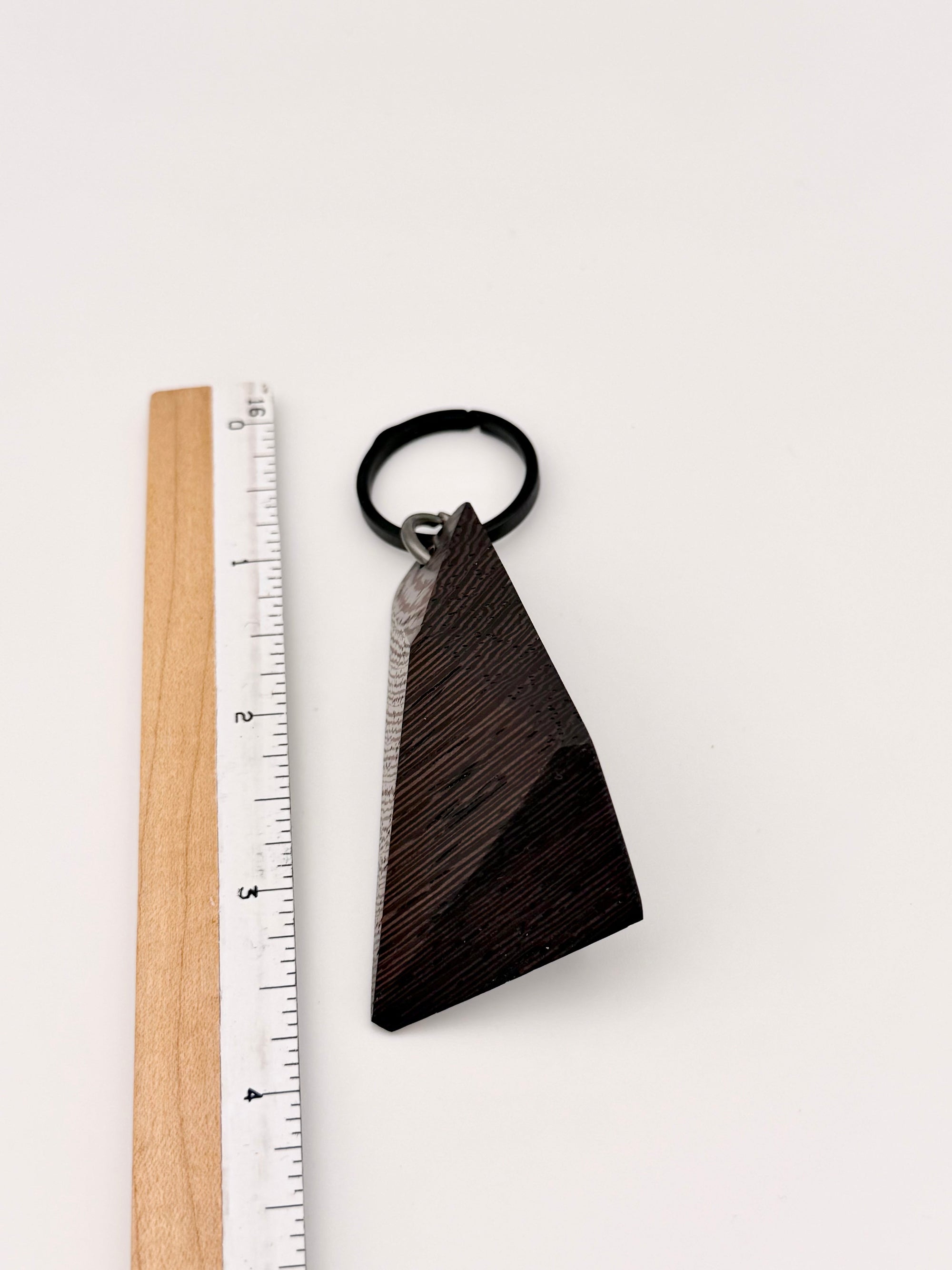 Wenge wood triangular keychain next to a ruler on a white background