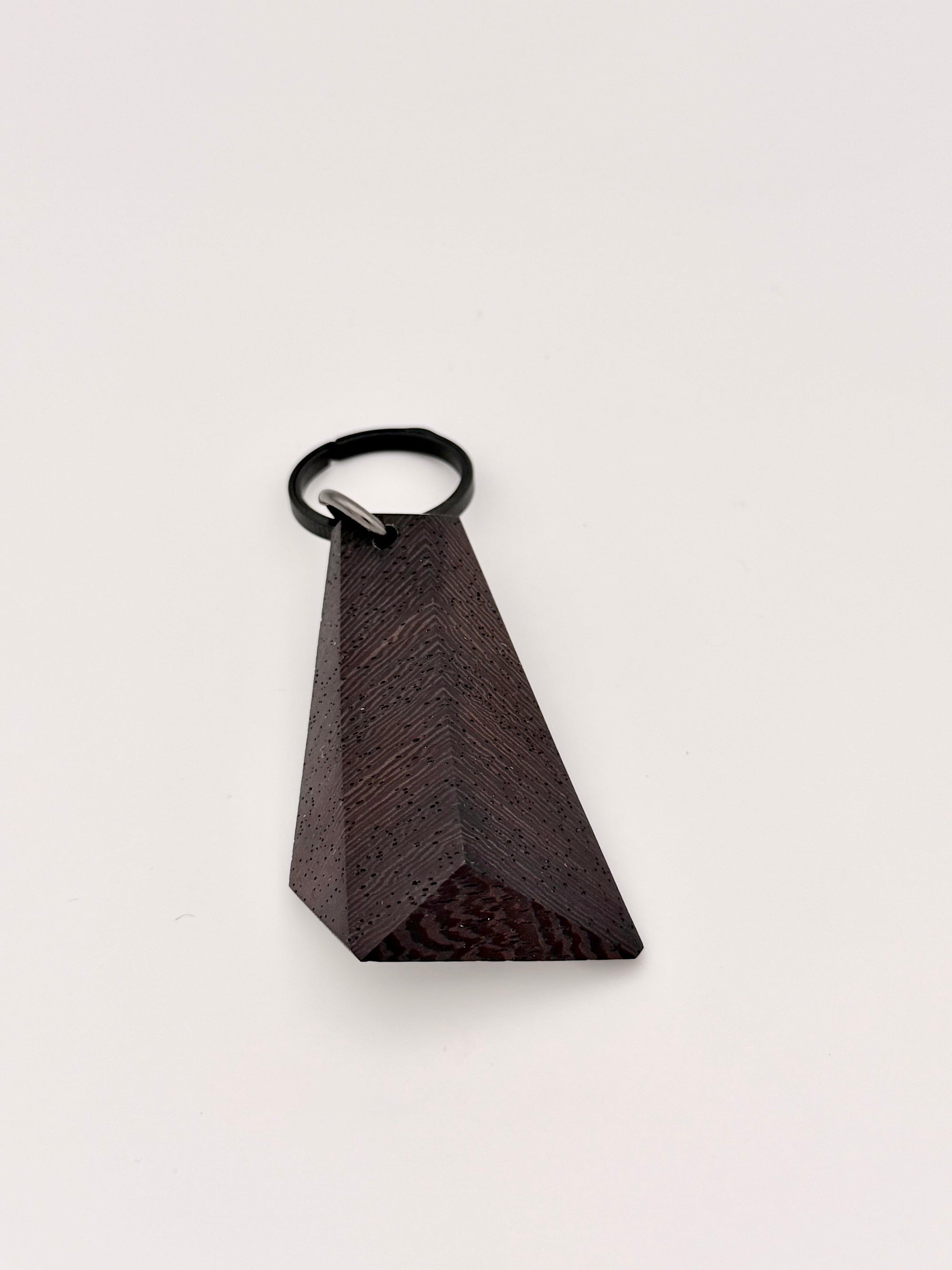 Black triangular wood faceted object with a black titanium key ring on a light gray background