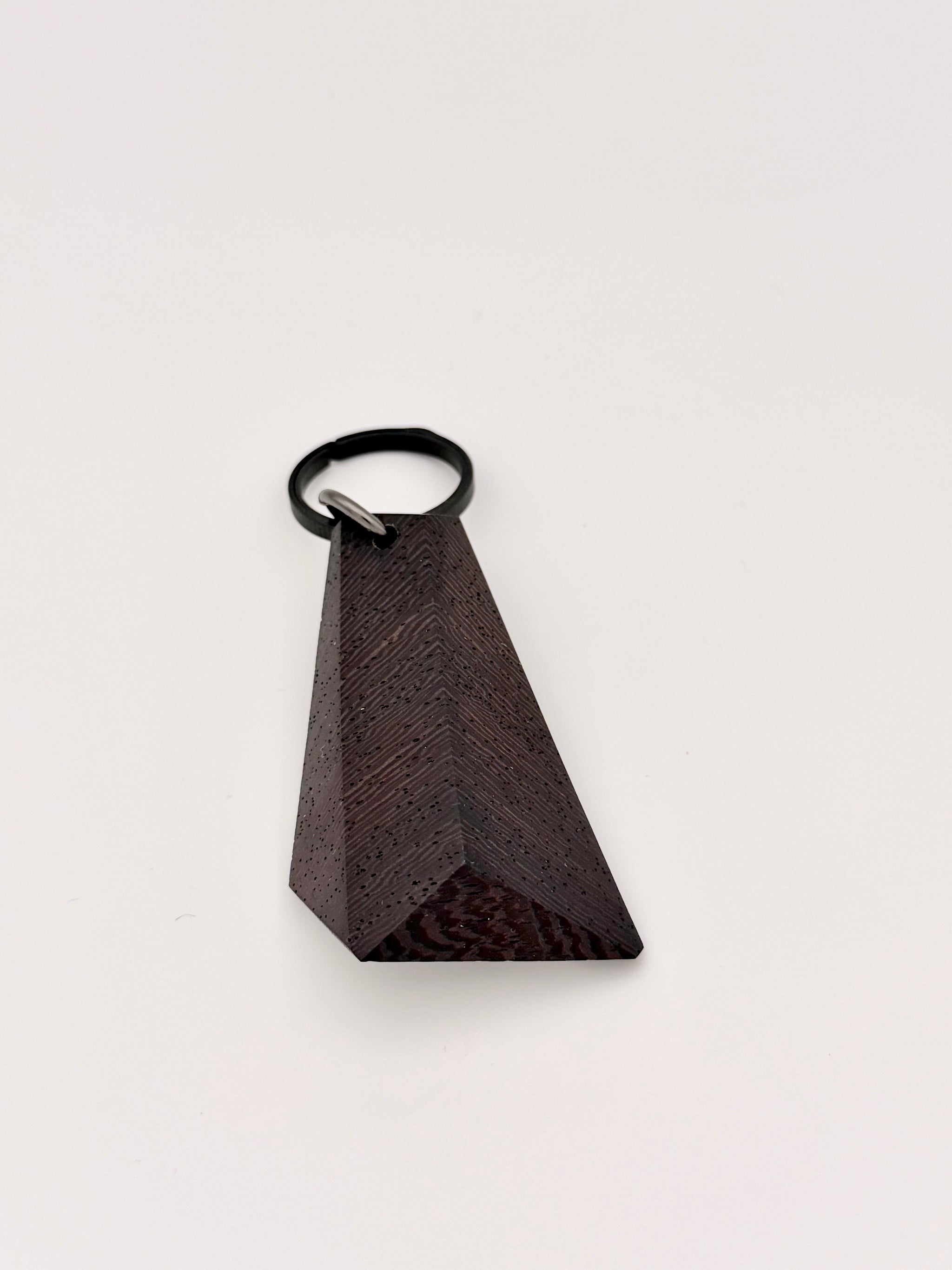 Black triangular wood faceted object with a black titanium key ring on a light gray background