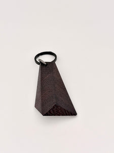 Black triangular wood faceted object with a black titanium key ring on a light gray background