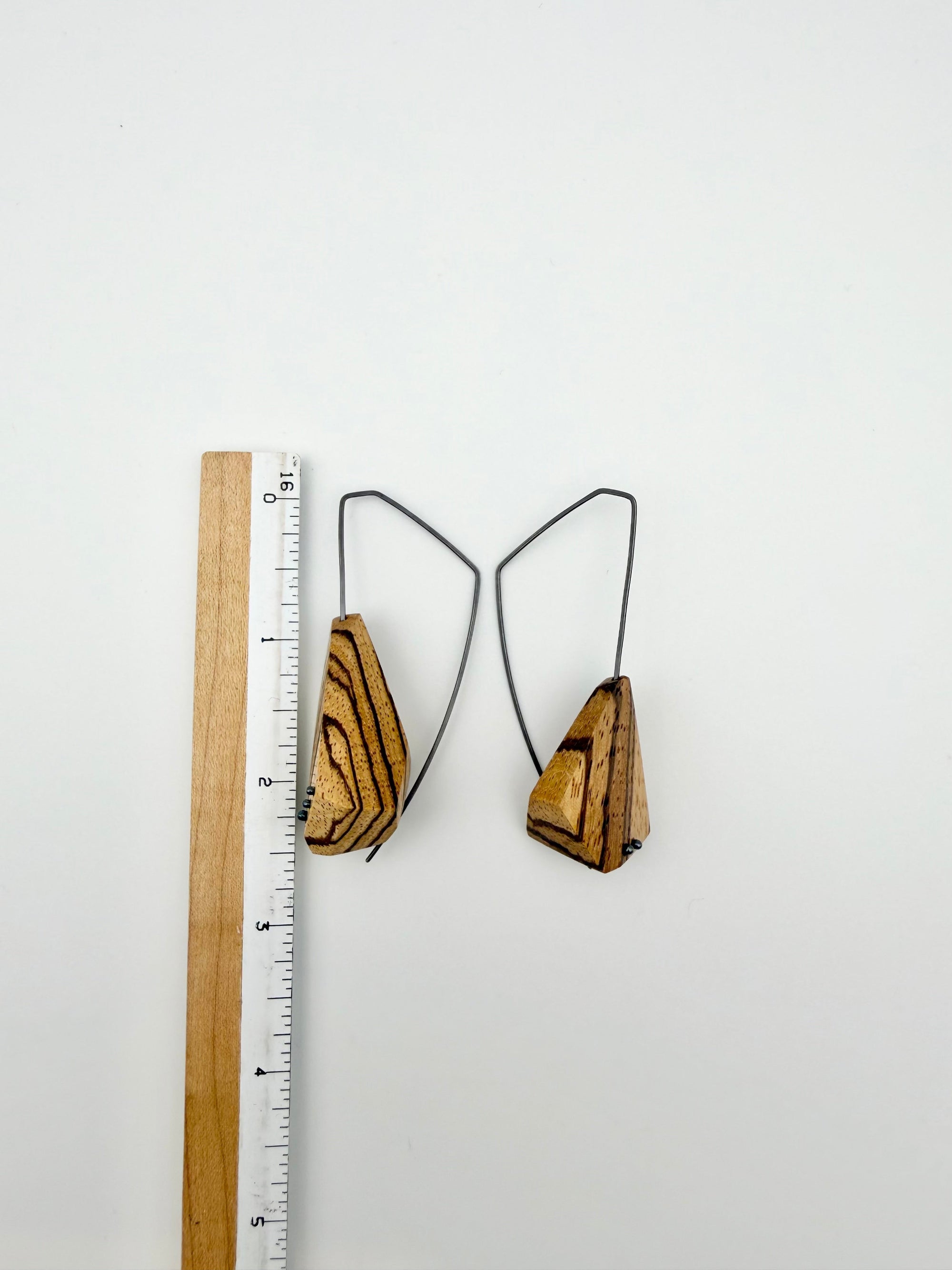 Wood earrings with dark ear wires next to ruler for scale. 