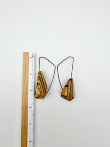 Wood earrings with dark ear wires next to ruler for scale. 