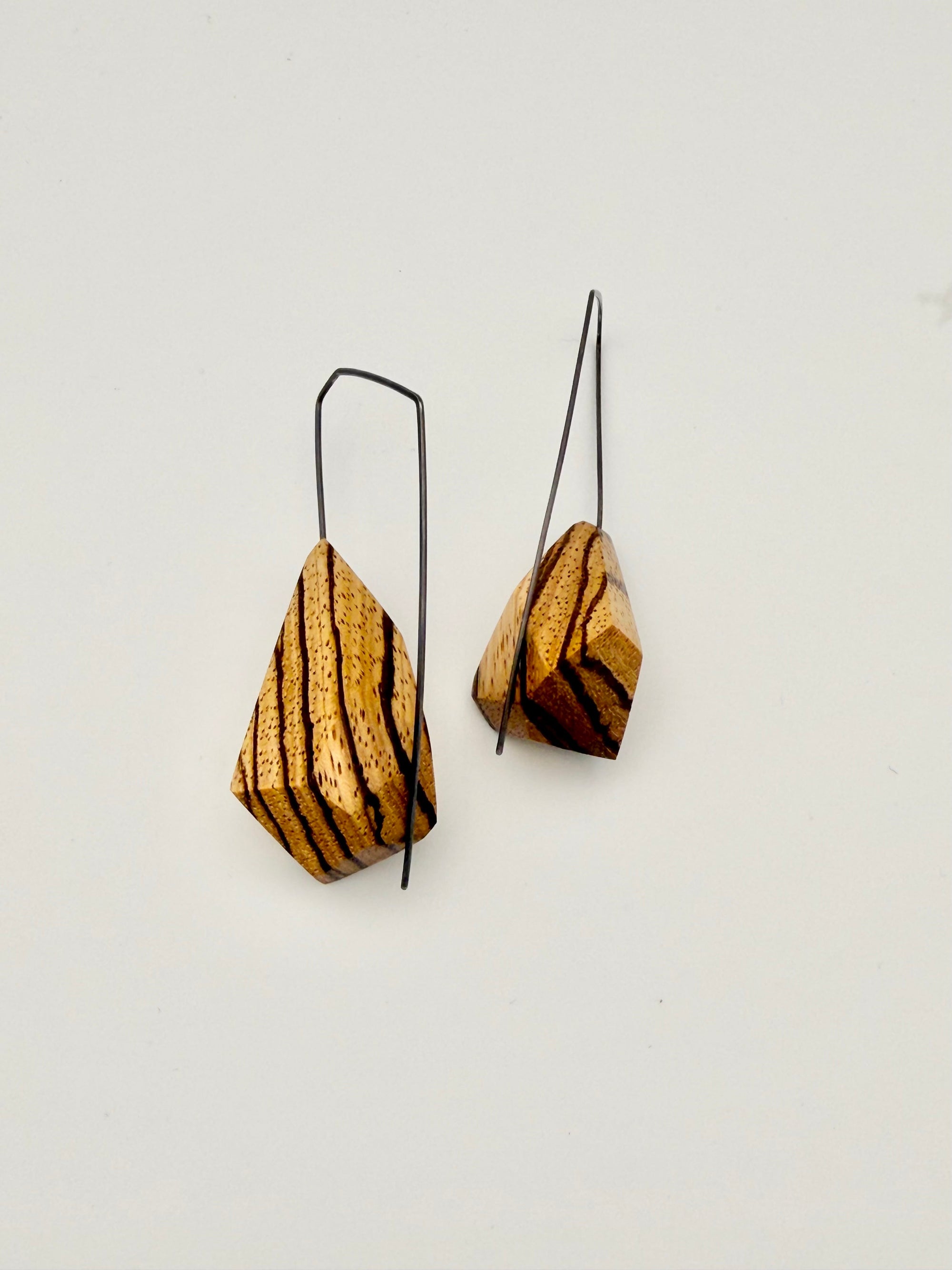Back view of asymmetrical zebrawood earrings with oxidized angular hoops on a white background. 