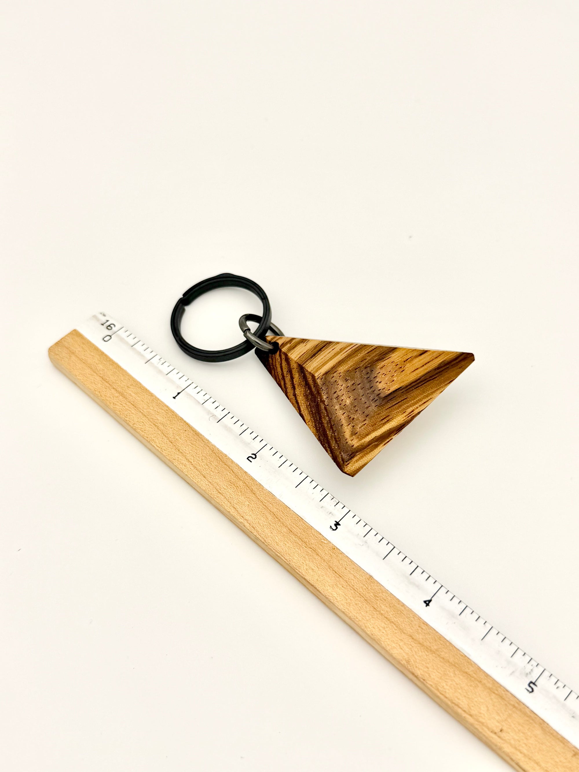 Wooden triangle keychain with a ruler for scale on a white background